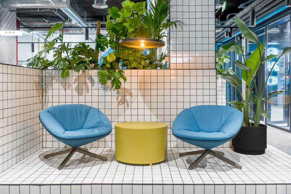 Modern co-living space at The Student Hotel Barcelona featuring stylish blue chairs, a yellow table, and vibrant plants.