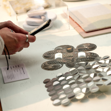 Hands examining reflective material samples at the Surface Design Show, showcasing innovative design concepts for 2023.