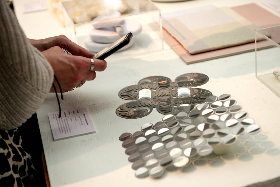 Hands examining reflective material samples at the Surface Design Show, showcasing innovative design concepts for 2023.