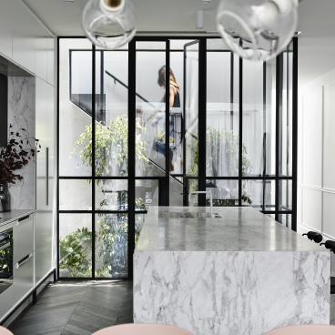 Modern kitchen featuring marble countertops, sleek cabinetry, and Parisian-inspired glass doors that open to a lush garden.