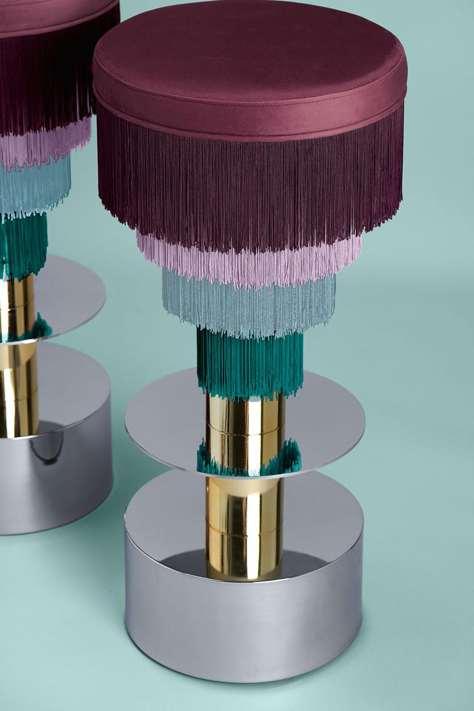 Stool designed by Masquespacio, featuring vibrant fringe layers in purple, teal, and silver, set against a mint background.
