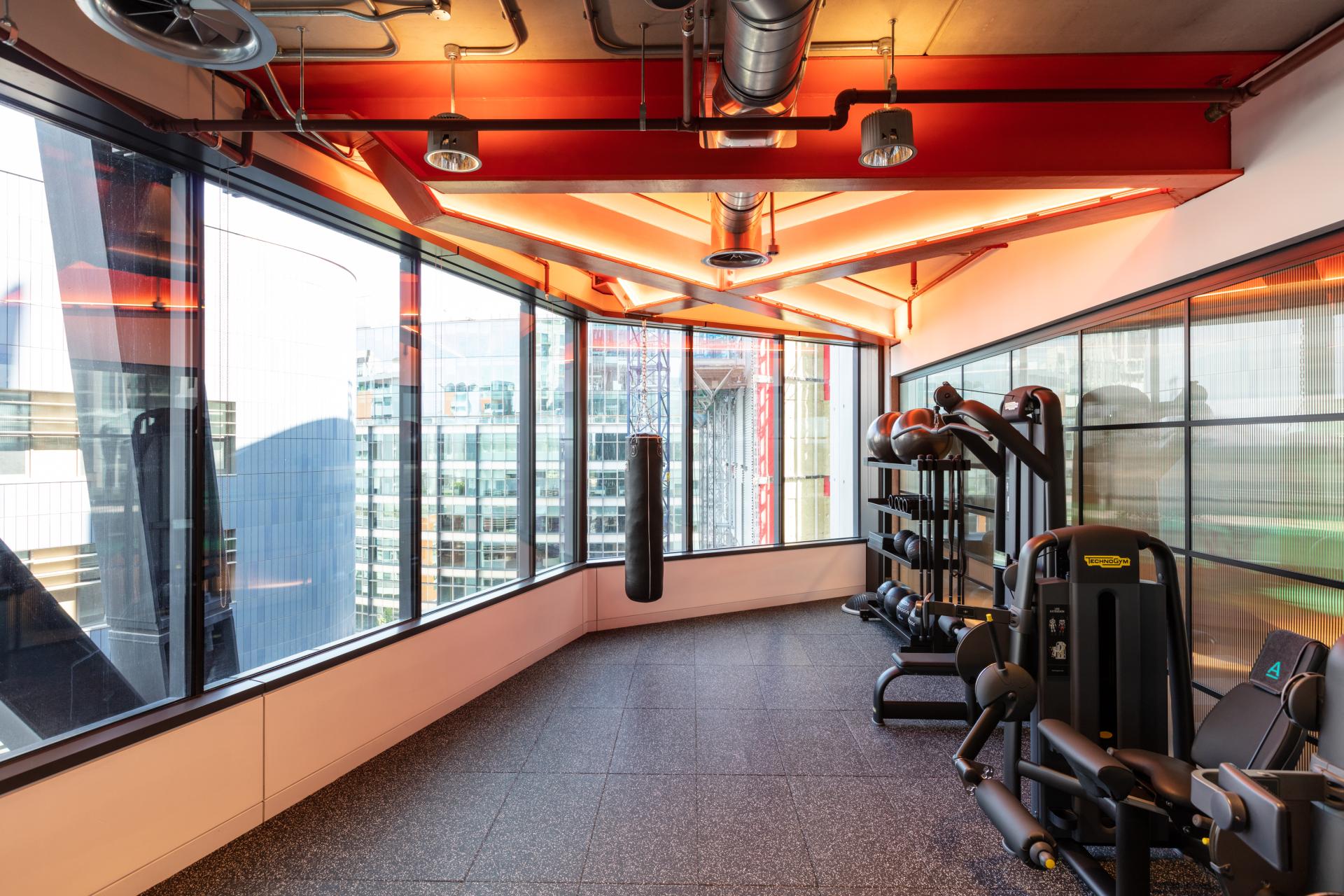 Bright, modern gym space with fitness equipment and large windows showcasing a vibrant urban view in Alpha FX London office.