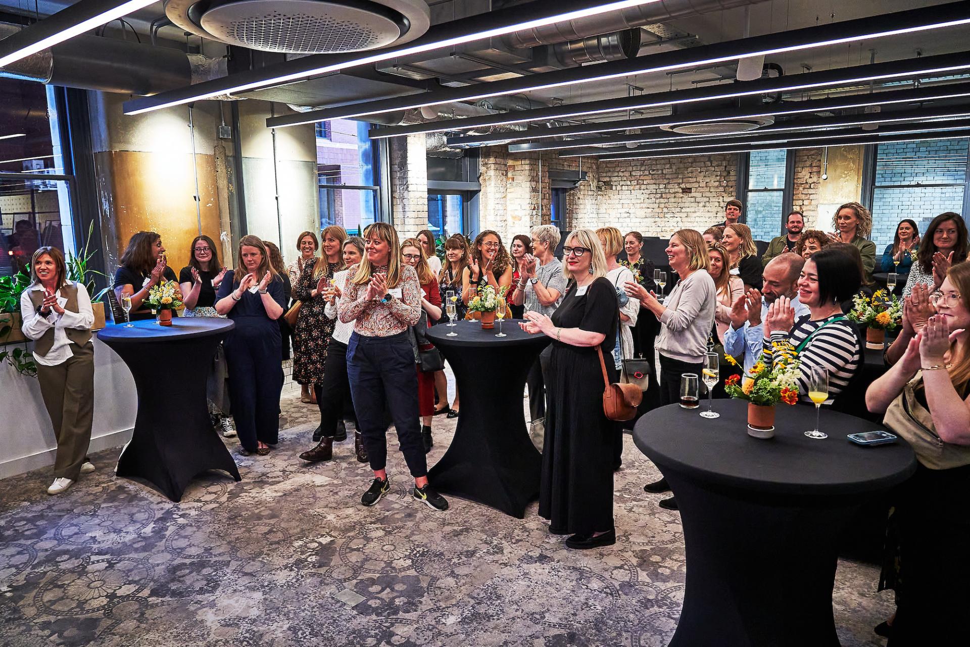 A diverse group of women and men celebrating at the 42 Gathering event, with floral decorations and drinks.