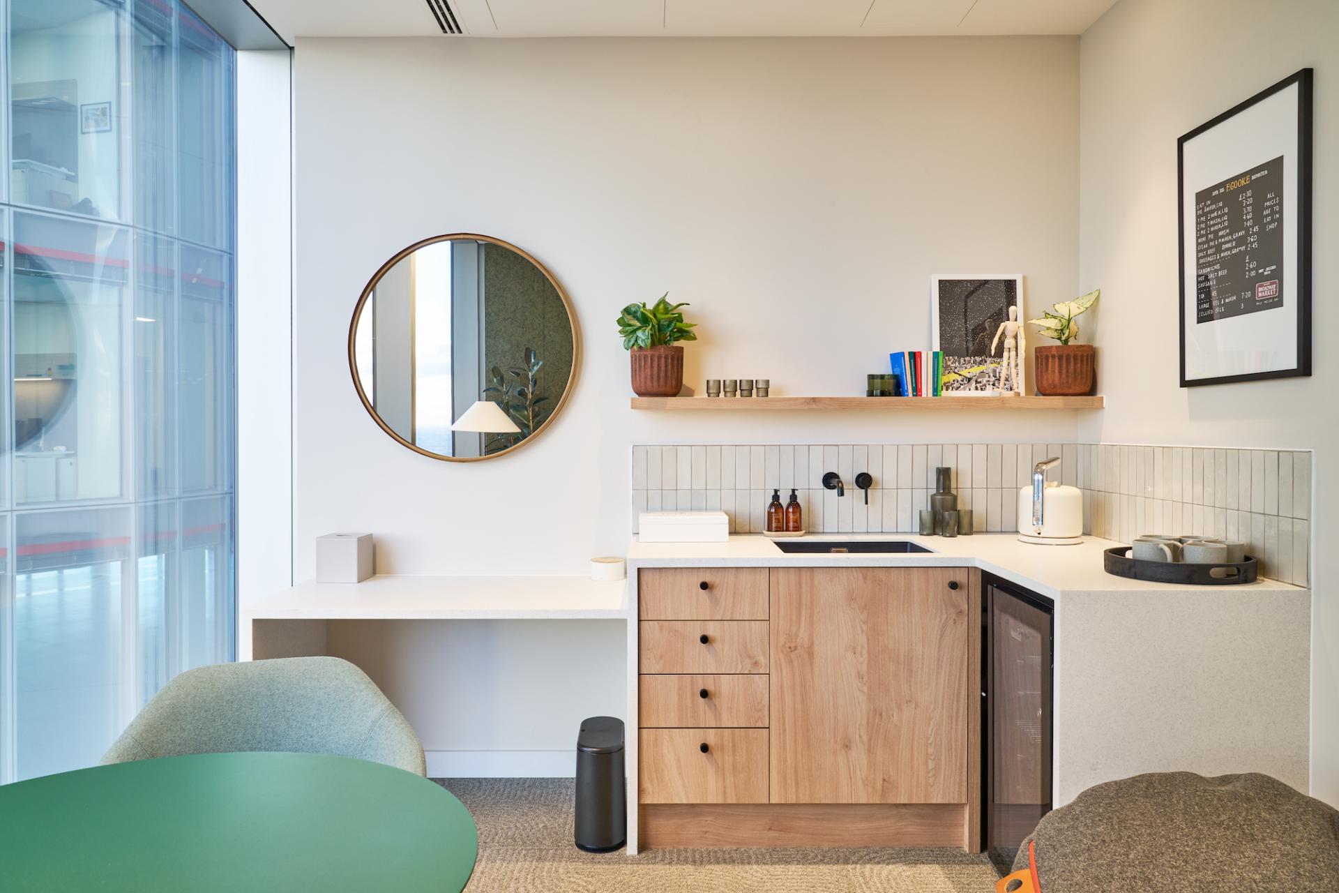 Modern workplace kitchenette featuring natural wood accents, a round mirror, plants, and a minimalist design for Bentley Systems.