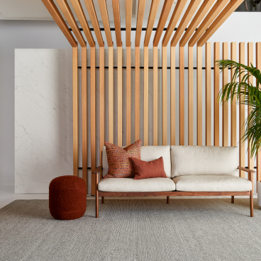 Modern interior featuring acoustic timber wall, stylish sofa with cushions, and a potted plant in a sophisticated setting.