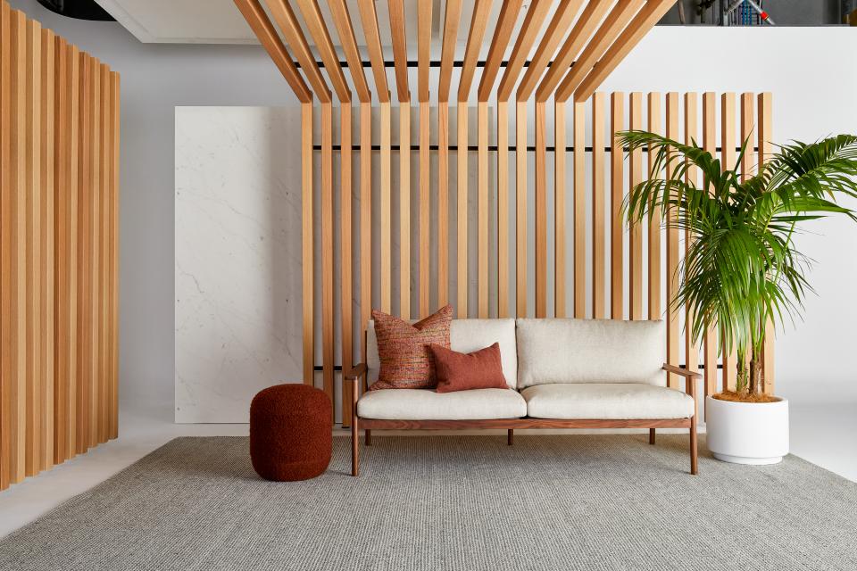 Modern interior featuring acoustic timber wall, stylish sofa with cushions, and a potted plant in a sophisticated setting.