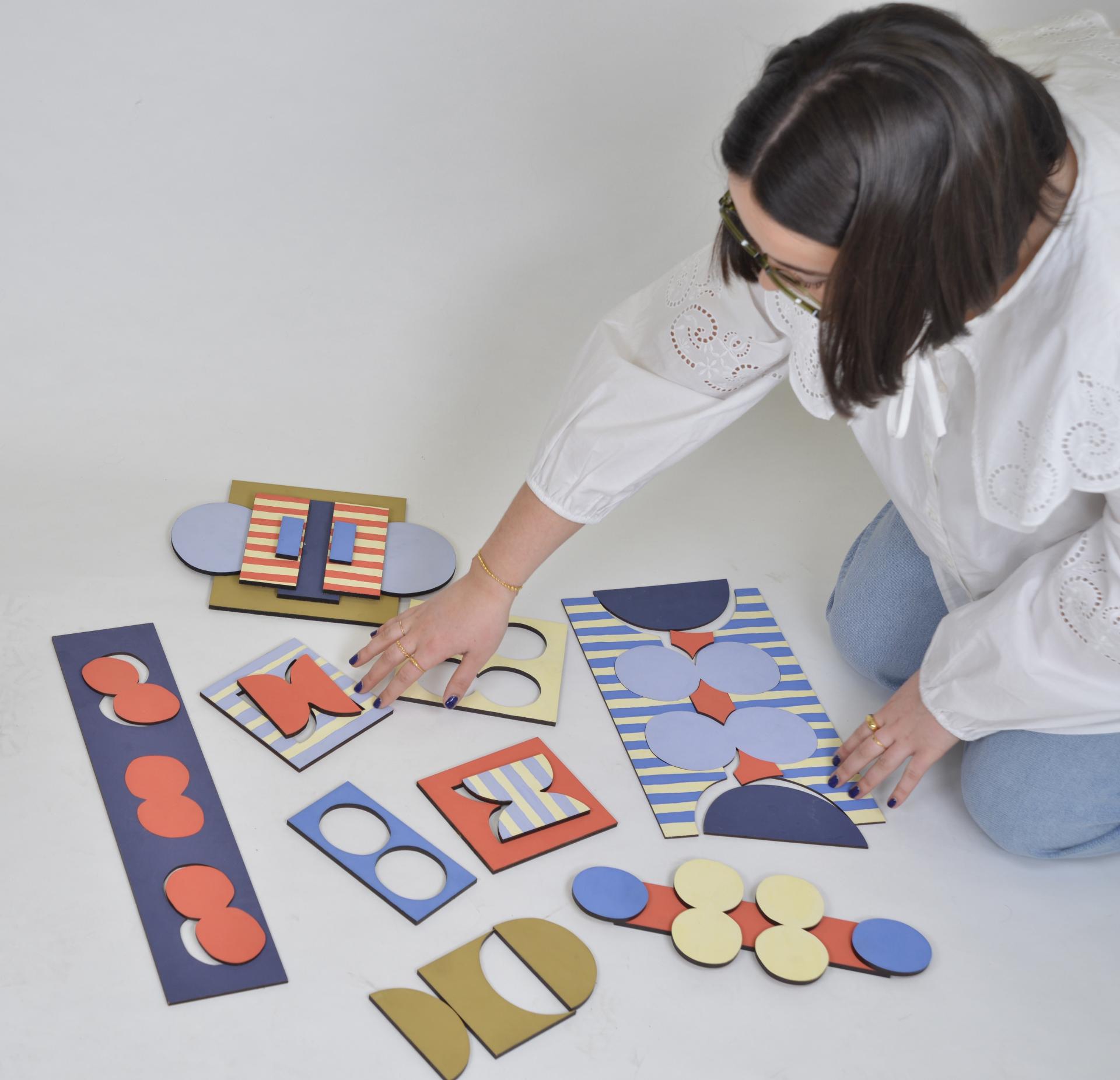 A woman arranging colorful geometric shapes and designs on a white surface, reflecting creativity at the Manchester School of Art.