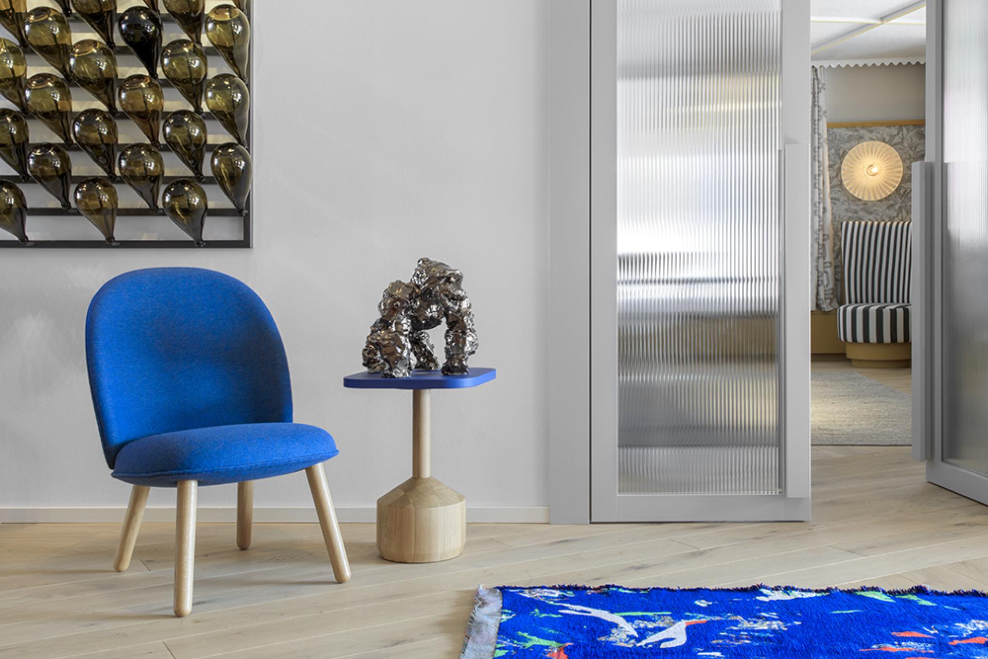 Modern blue chair with artistic sculpture and vibrant rug, showcasing stylish alpine design aesthetics at Icaro Hotel.