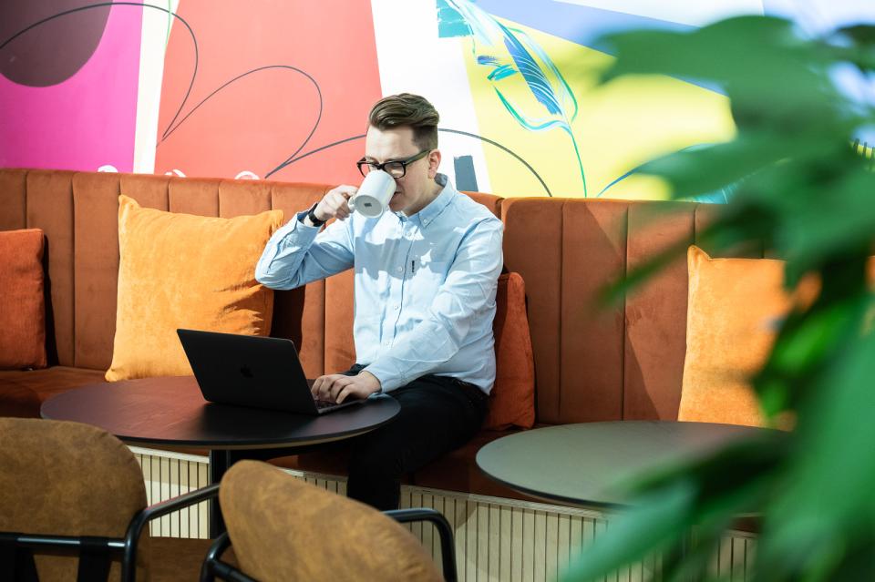 Young man sipping coffee while working on a laptop in a vibrant, colorful co-working space designed by Sheila Bird Studio.
