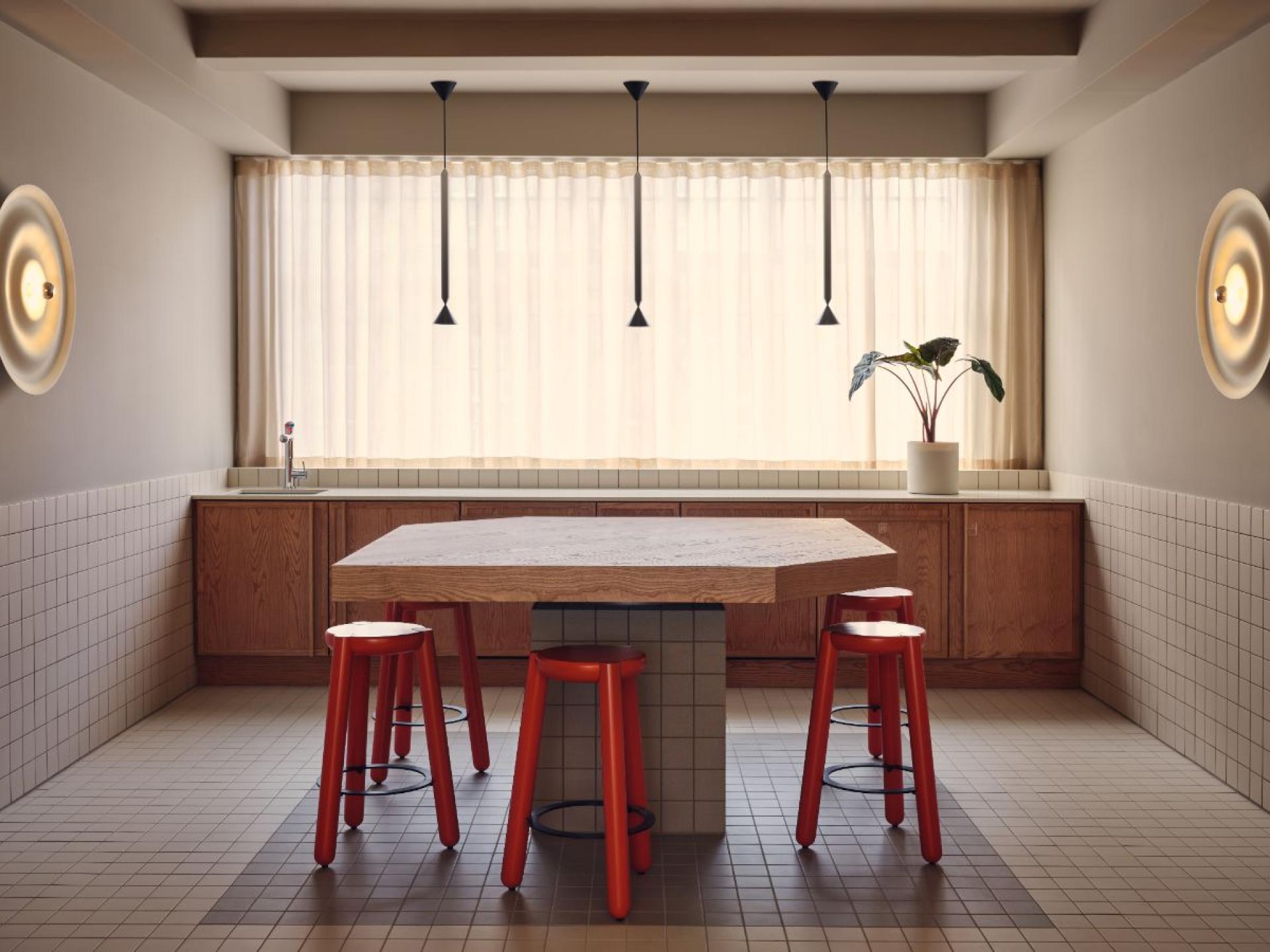 Modern flexible workspace kitchen featuring an oak island, red stools, natural light, and minimalist decor in London.