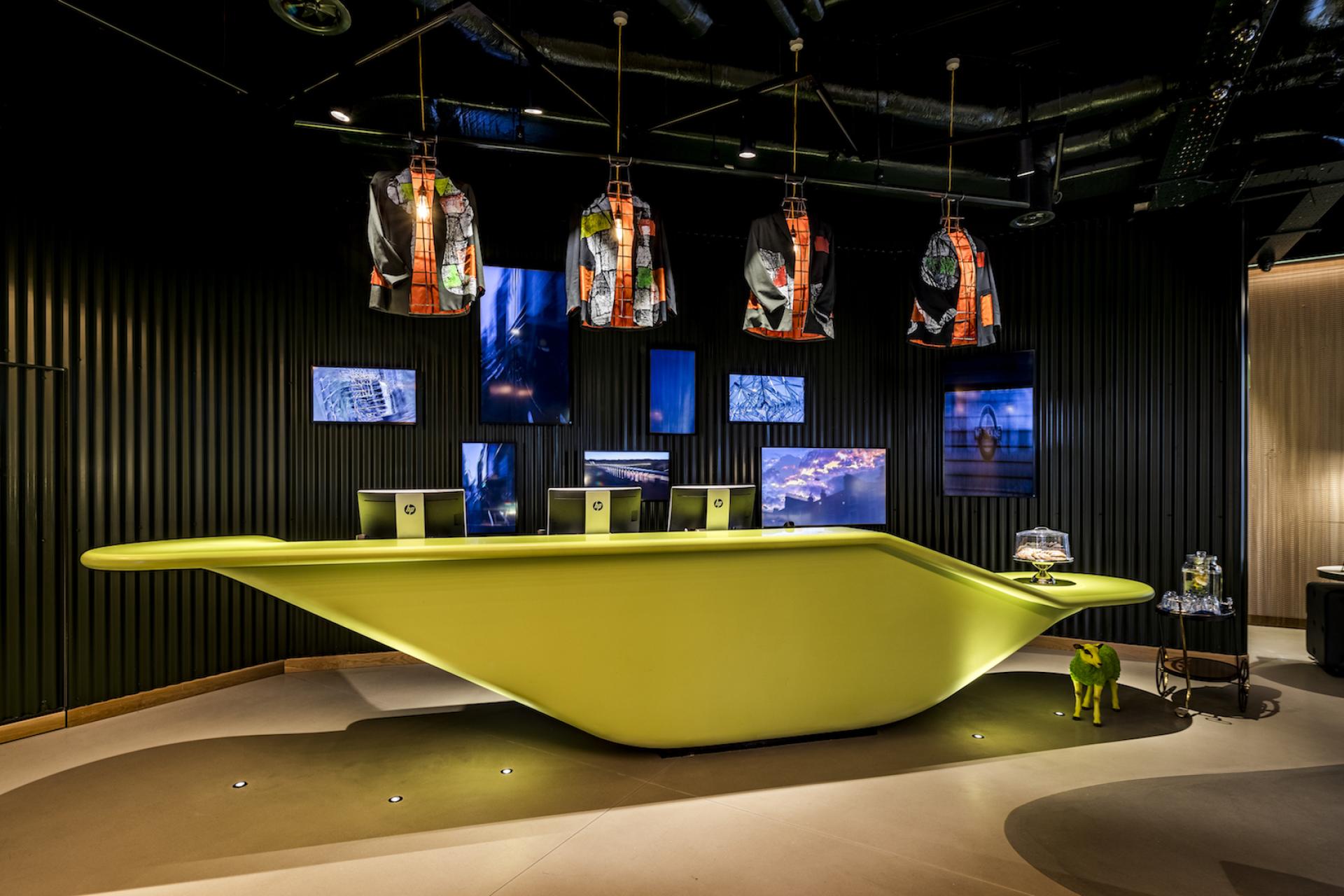 Stylish hotel reception area at nhow London featuring vibrant green desk and artistic hanging decor.