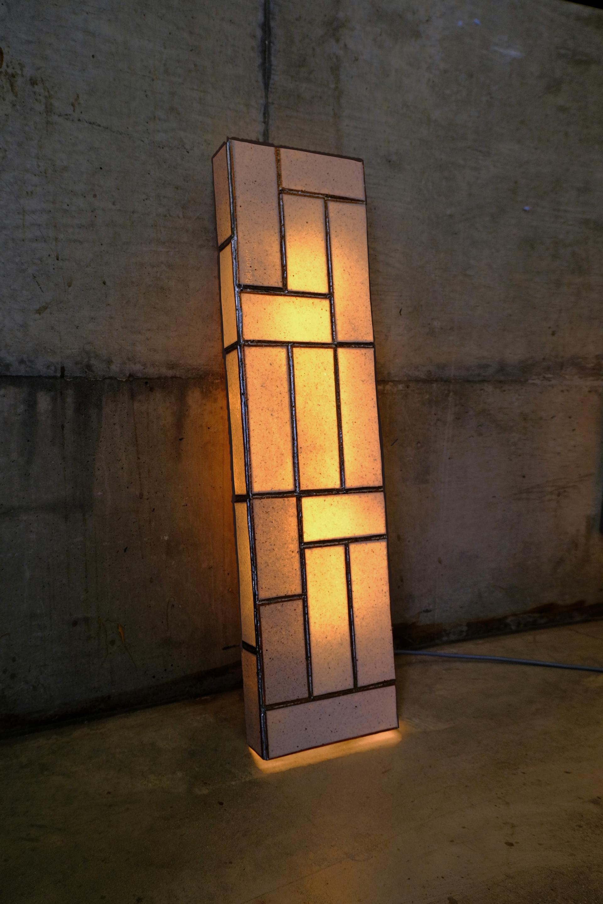 Sleek, modern lamp made from recycled ceramic and waste ash, illuminating a minimalist space with warm light.