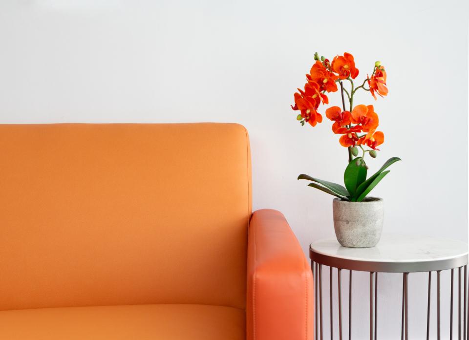 Bright orange Ultraleather® couch beside a modern table with an orange floral arrangement, showcasing stylish interior design.