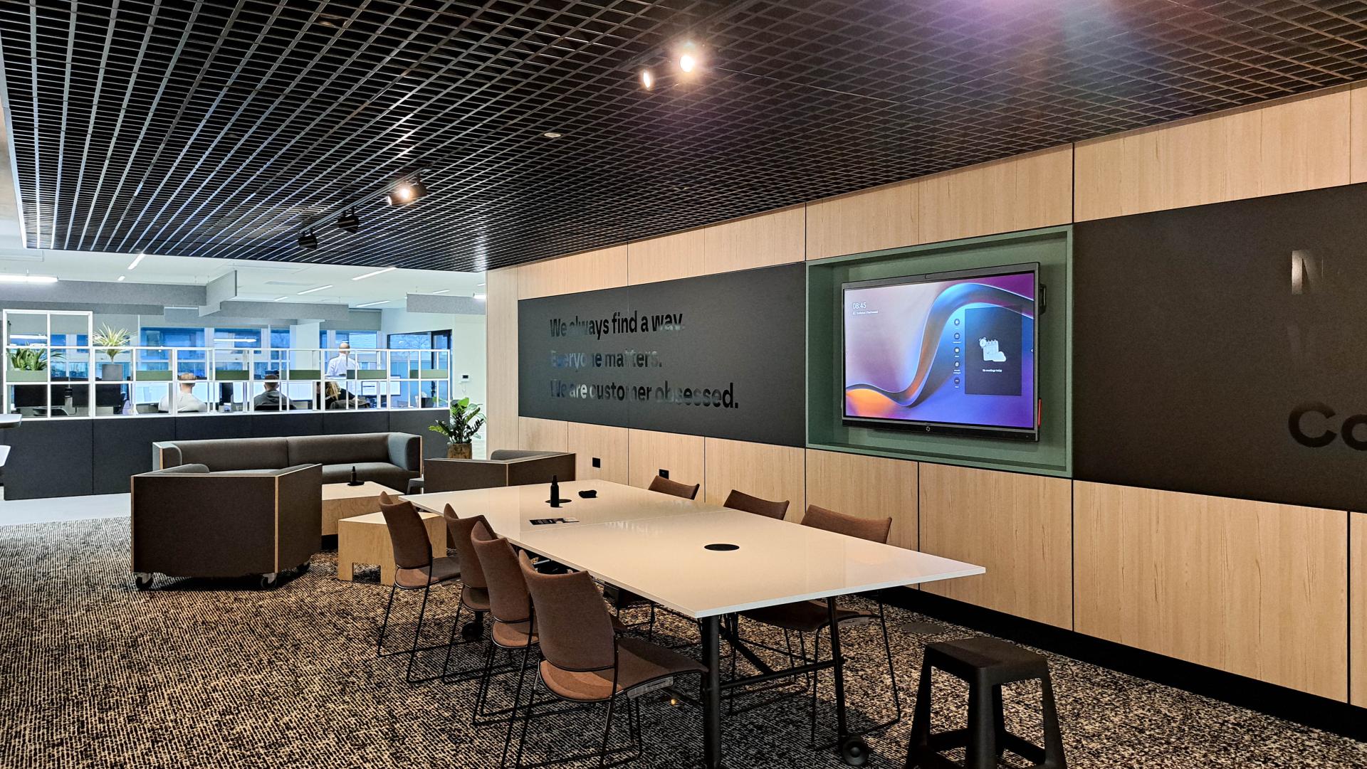 Modern office interior featuring a collaborative workspace with a large table, seating area, and integrated technology for interactions.
