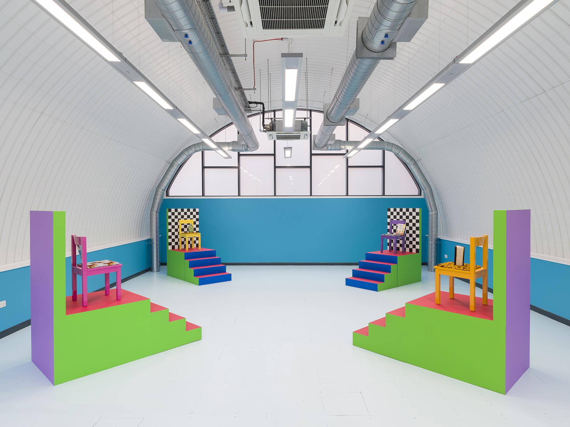 Vibrant display of colorful chairs on platform steps showcasing contemporary design at London Craft Week 2019.