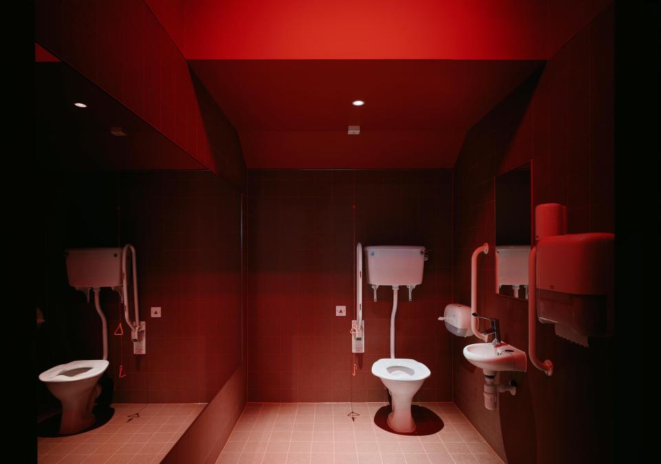 Modern restroom interior featuring bold red lighting, sleek fixtures, and textured tile at Sedbergh School's Queens Hall.
