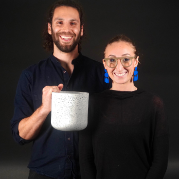 Elizabeth Bridges and Garrett Benisch showcase sustainable biomaterials with a speckled container, highlighting eco-friendly innovations.