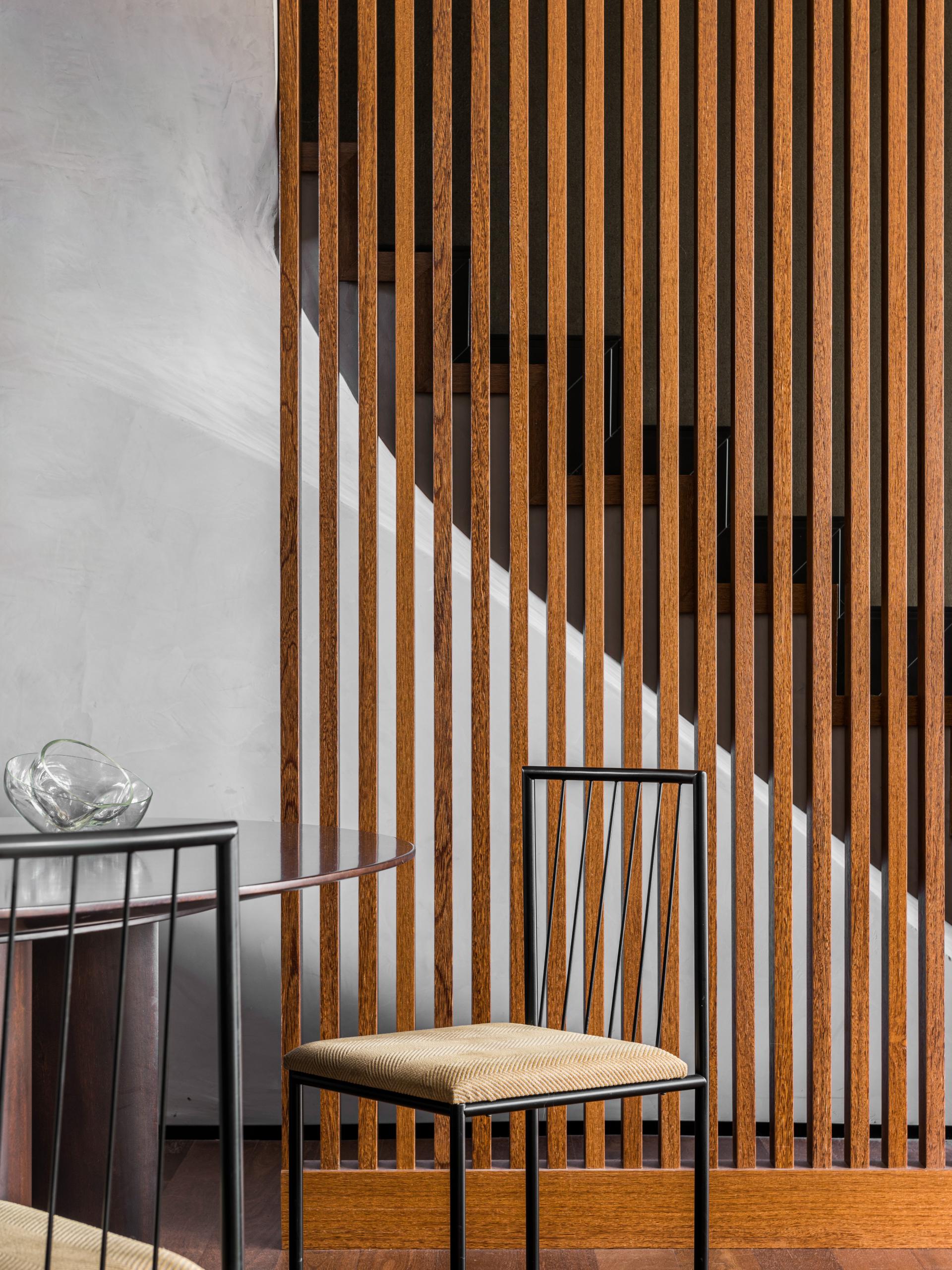 Elegant wooden slats feature prominently in Apto Paulista's interior design, framing an inviting dining space with modern furnishings.