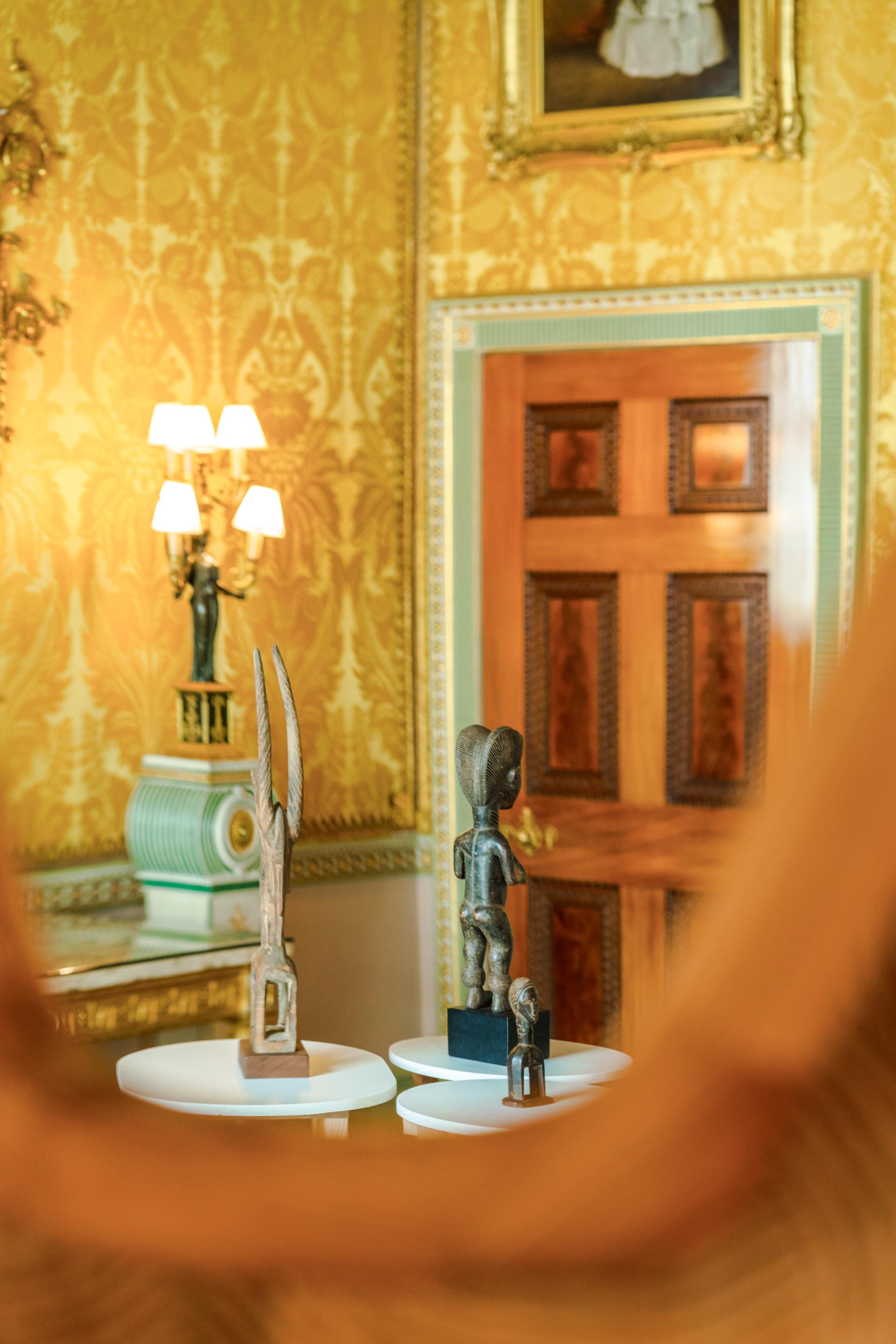 Artistic sculptures displayed on pedestals in an elegantly decorated room featuring gold wallpaper and vintage decor.
