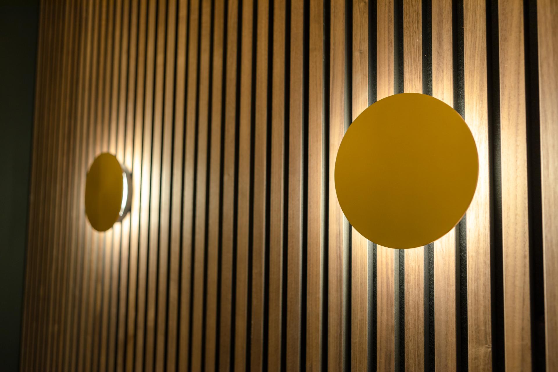 Modern wall lamps illuminate a wooden slatted wall, showcasing Eatock Design & Build’s innovative interior design.