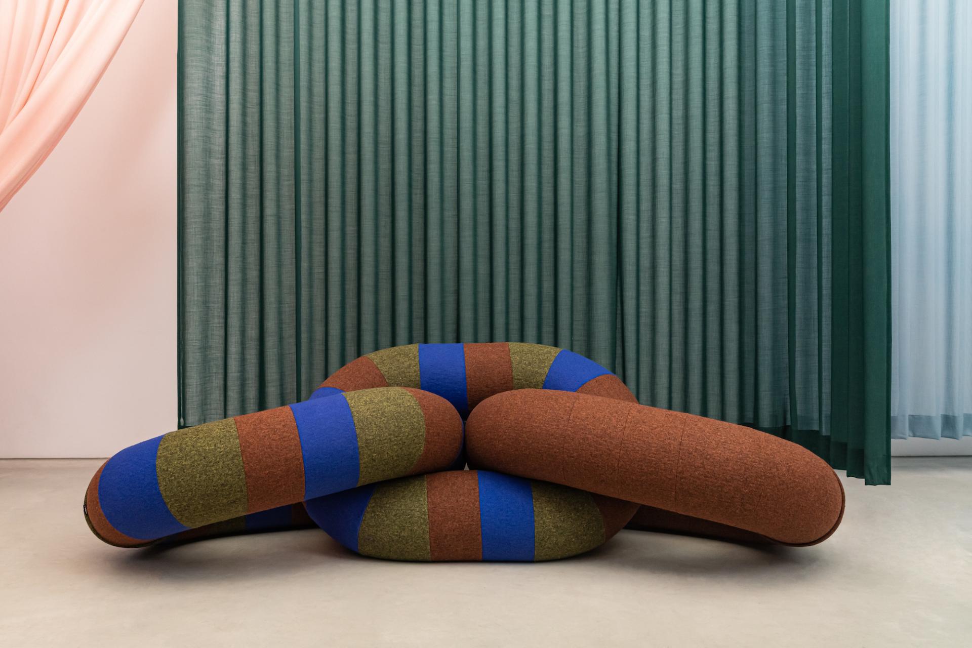 Colorful, sculptural seating arrangement against soft fabric drapes, showcasing innovative design trends from DDW 2023.