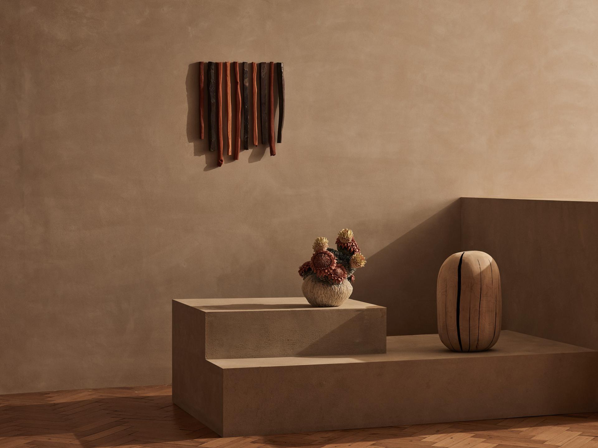 Contemporary craft display featuring textured wall art, a sculptural vase, and colorful floral arrangement in a minimalist setting.