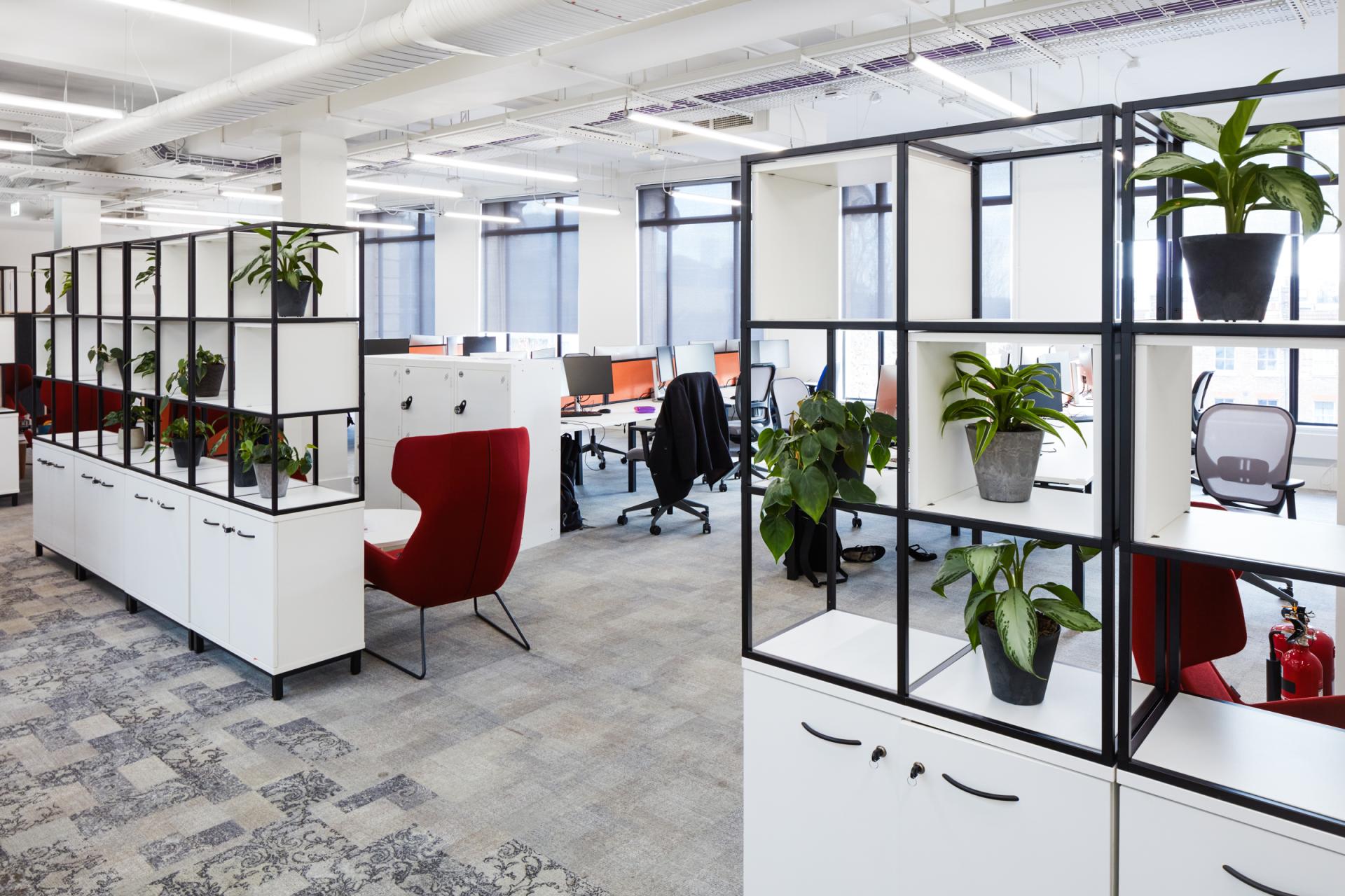 Modern office space at Queen Mary University of London featuring plants, workstations, and a red accent chair, designed for collaboration.