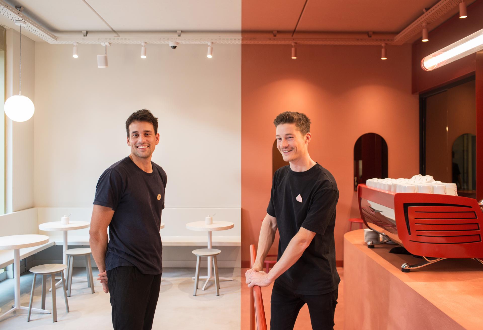 Two smiling baristas stand in a modern café, showcasing vibrant interior design with a coffee machine in a mixed-use space.