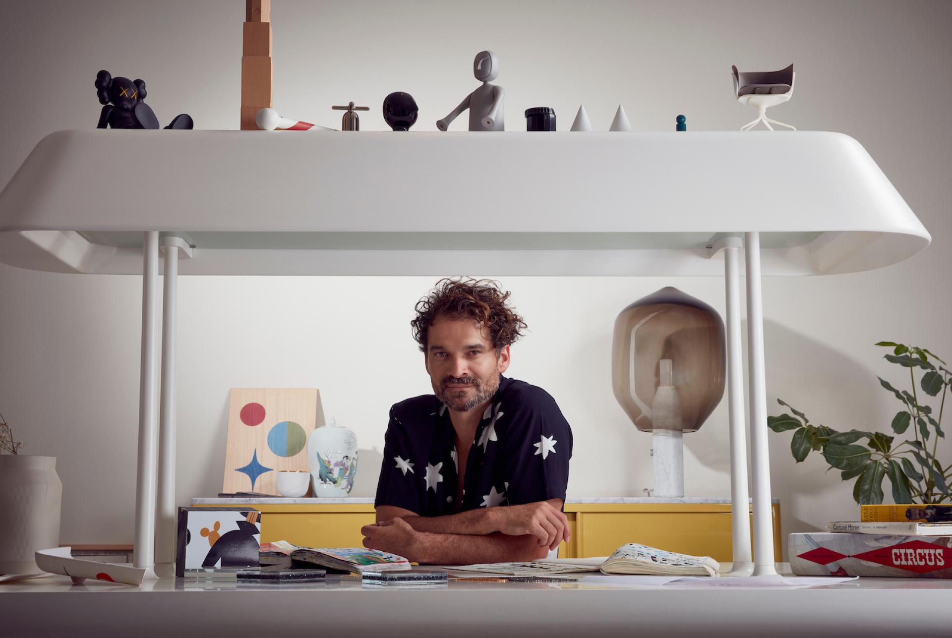 Jaime Hayon, renowned designer, poses at his creative workspace featuring colorful art pieces and unique decor elements.