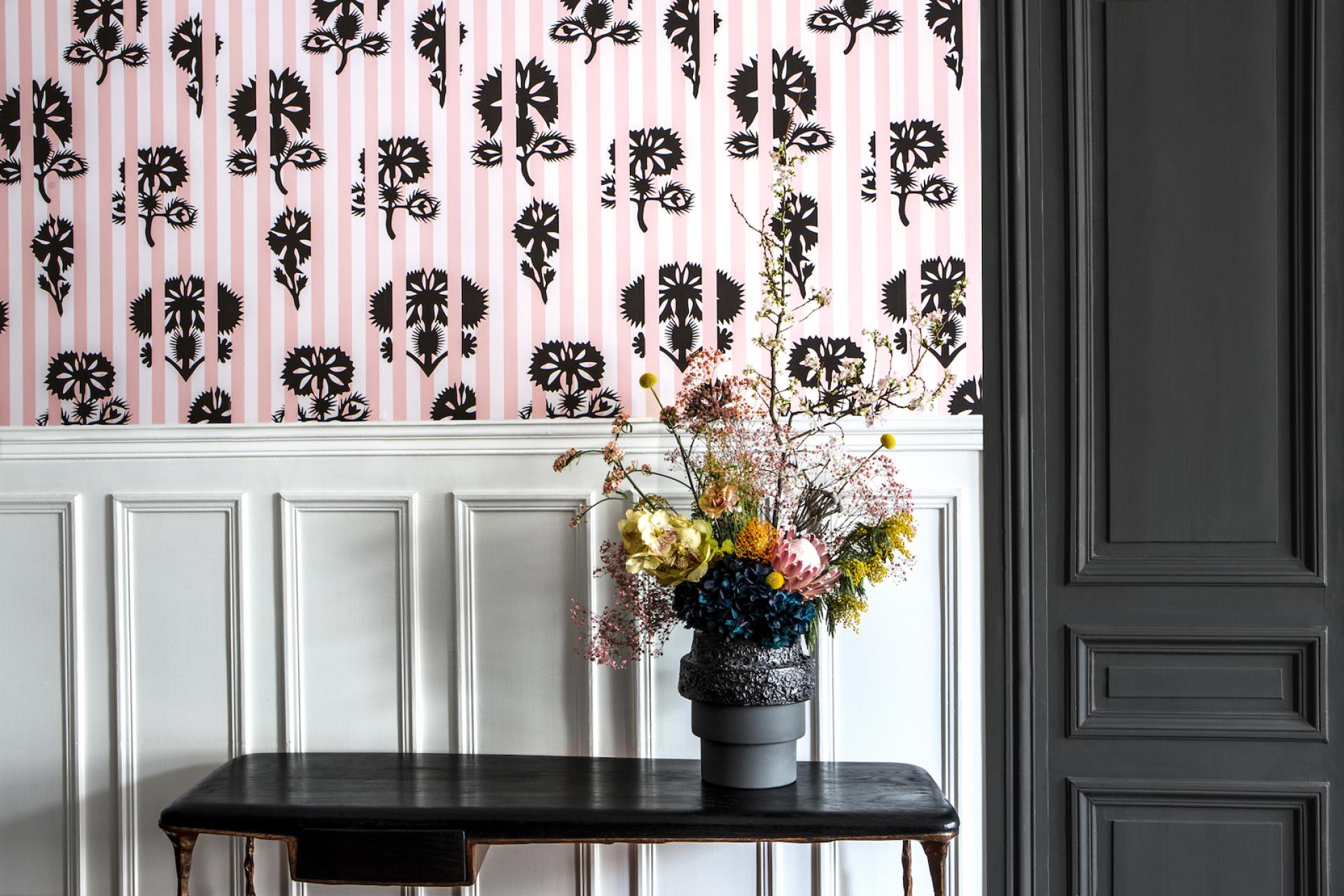 Bold floral wallpaper design by Graham & Brown, featuring black motifs on a pink striped background with a stylish bouquet in the foreground.