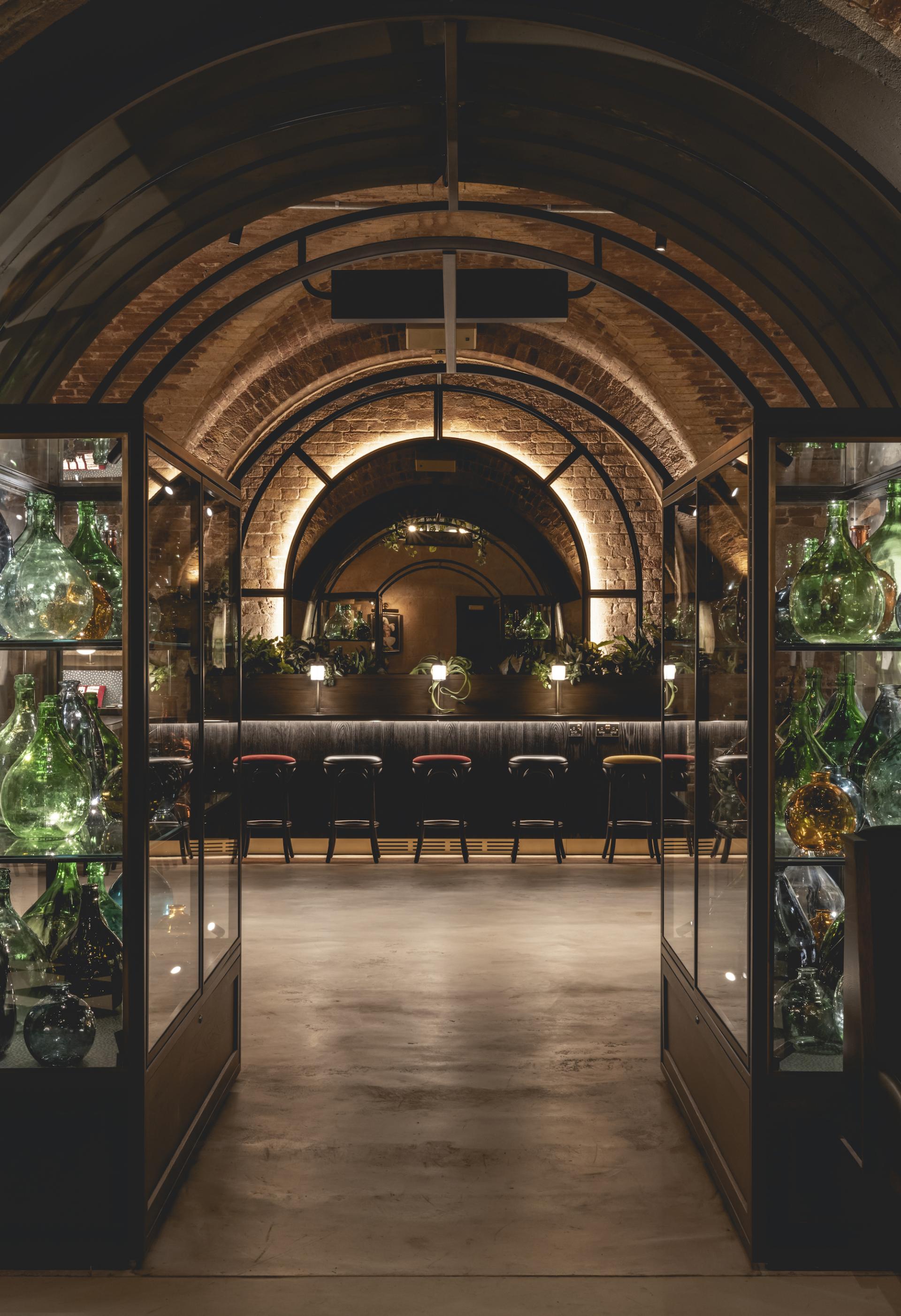 Interior view of The Libertine, featuring illuminated brick arches, a bar, and decorative glassware displays.