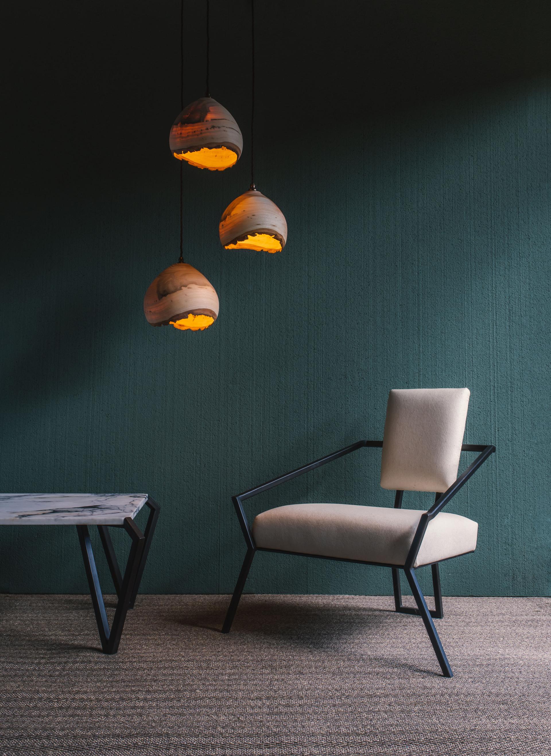 Elegant cream chair beside a modern marble-topped table and artistic pendant lights in a stylish interior setting.