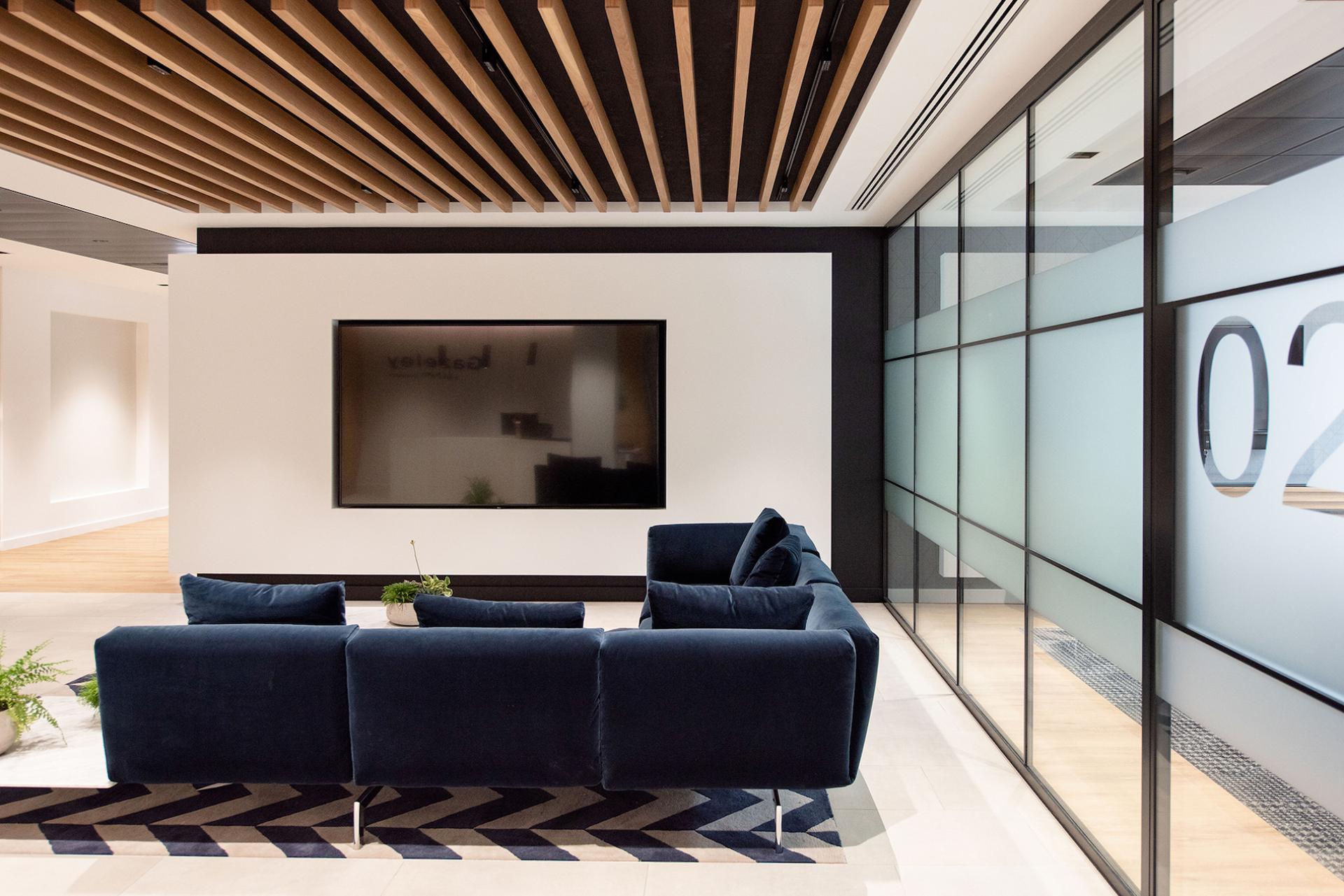 Modern office lounge featuring a navy blue sofa and sleek wood-beamed ceiling, reflecting contemporary workplace design.