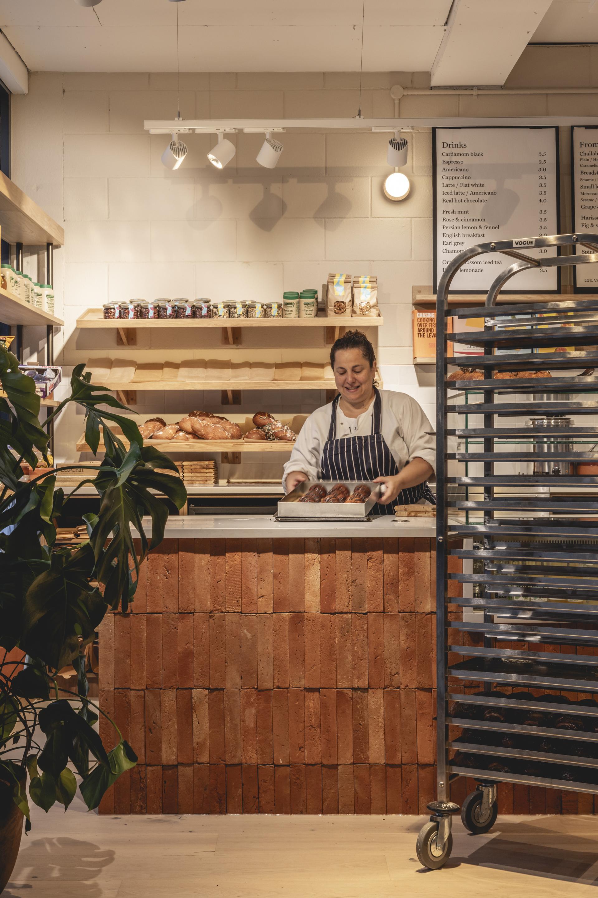 Chef preparing freshly baked goods at Honey & Co’s deli, featuring warm terracotta textures and inviting interior design.