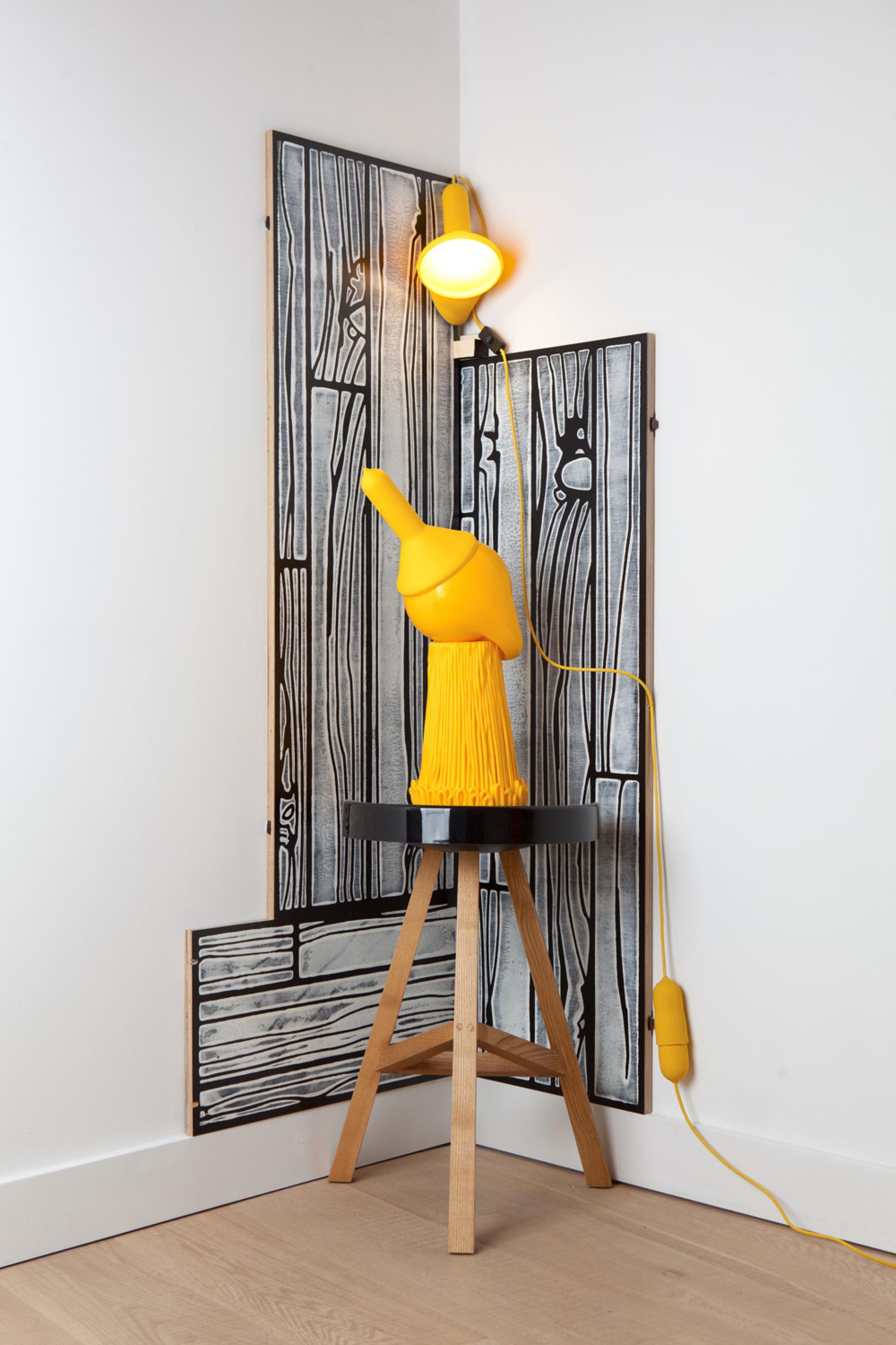 Bright yellow sculpture resembling a mop stands on a black stool against patterned wood paneling, showcasing Lorenzo Vitturi's artistic design.