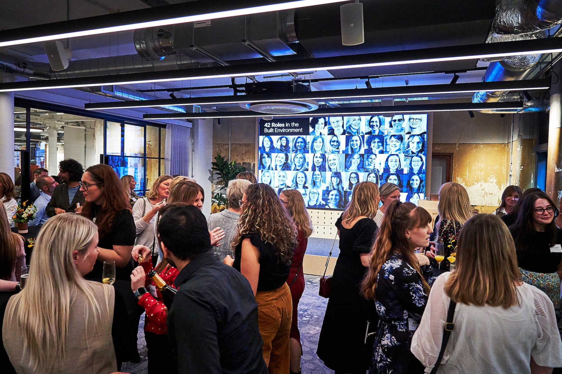 Celebration gathering for the podcast "42 Roles in the Built Environment" with attendees socializing and a display of featured guests.