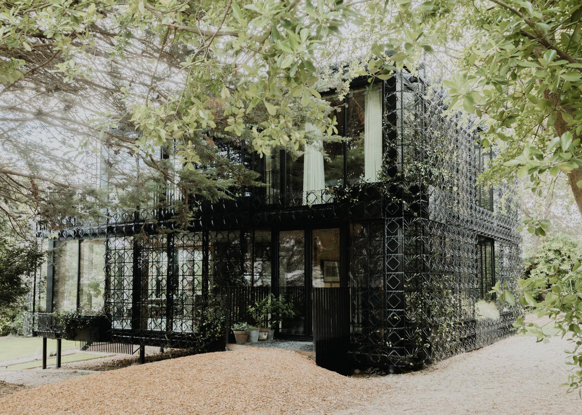 Woven by Giles Miller Studio features a unique black sculptural facade surrounded by lush greenery in a residential setting.