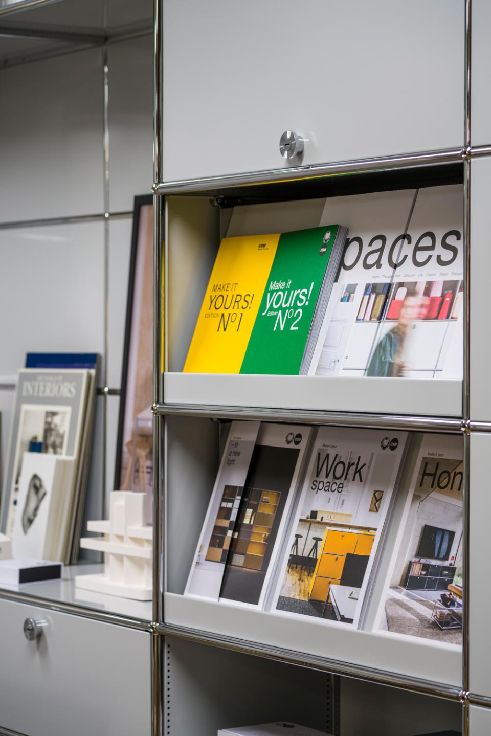Colorful magazines showcasing USM furniture designs displayed on a sleek modular shelving unit in the Clerkenwell showroom.