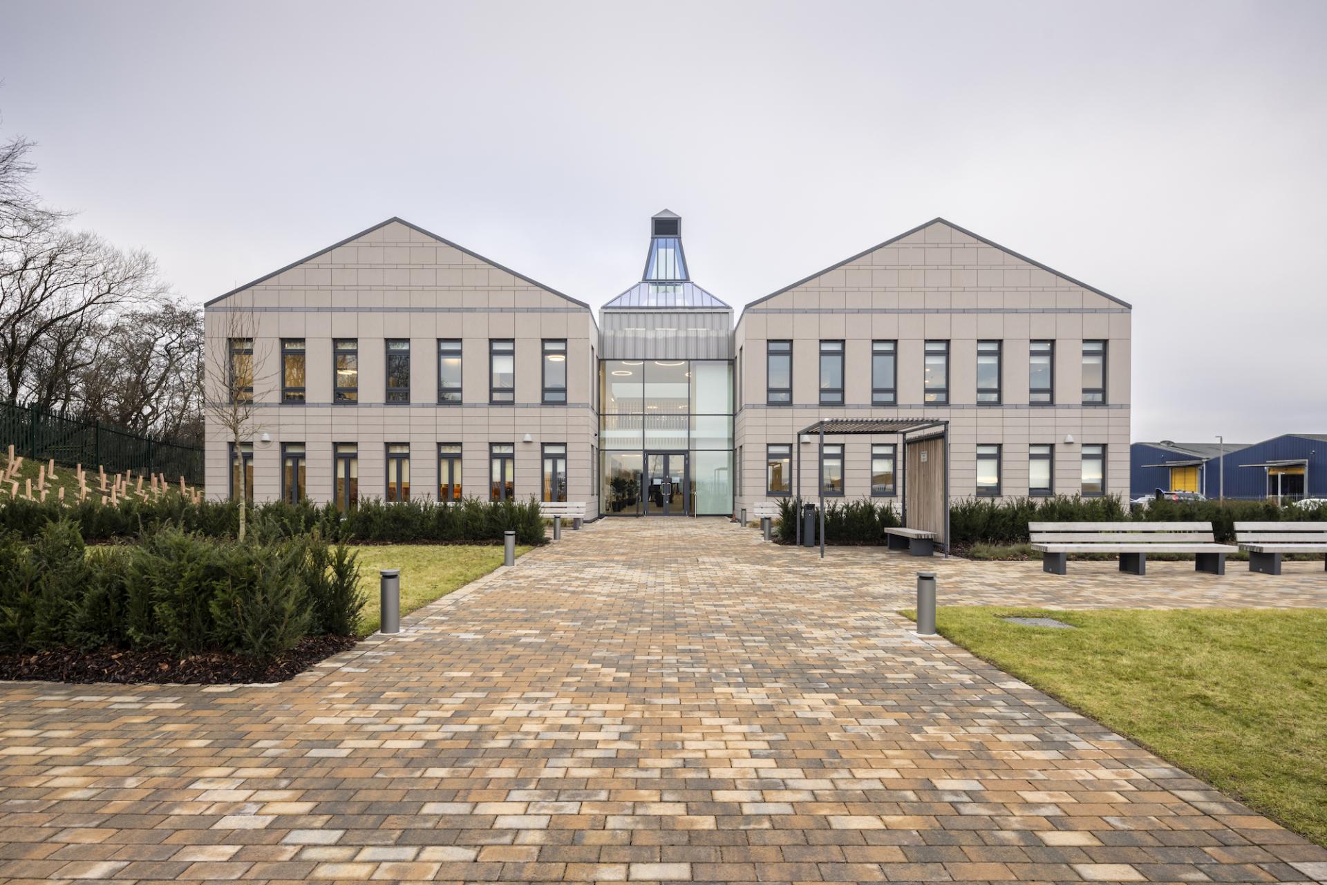 Modern office building of Ian Macleod Distillers surrounded by greenery, featuring a landscaped pathway and large glass entrance.