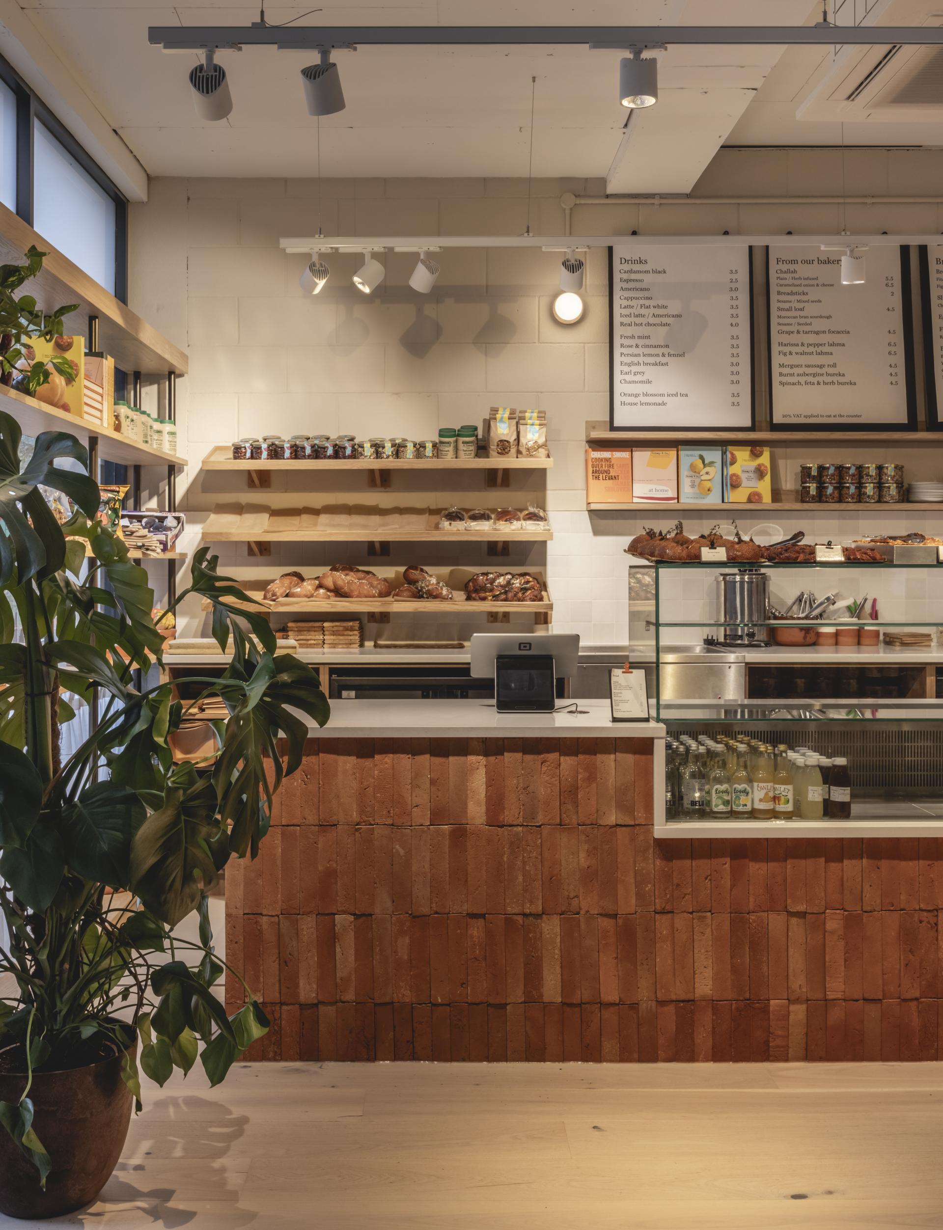 Deli counter at Honey & Co showcasing terracotta textures, fresh baked goods, and a variety of beverages in a cozy interior.