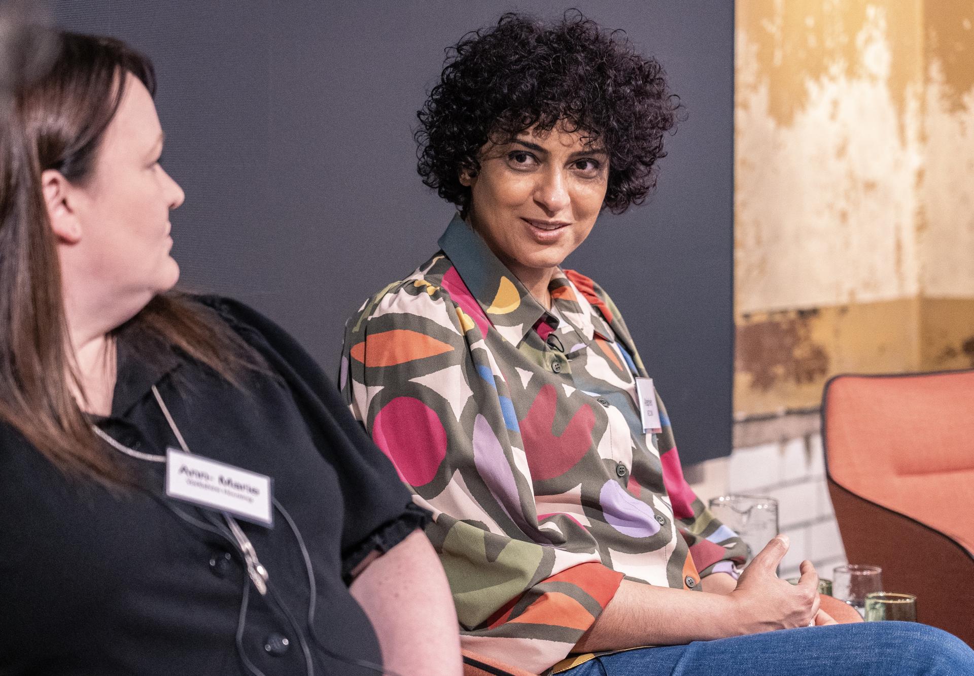 Two women engage in a lively discussion on technology, showcasing diverse perspectives at the Material Source Studio event.