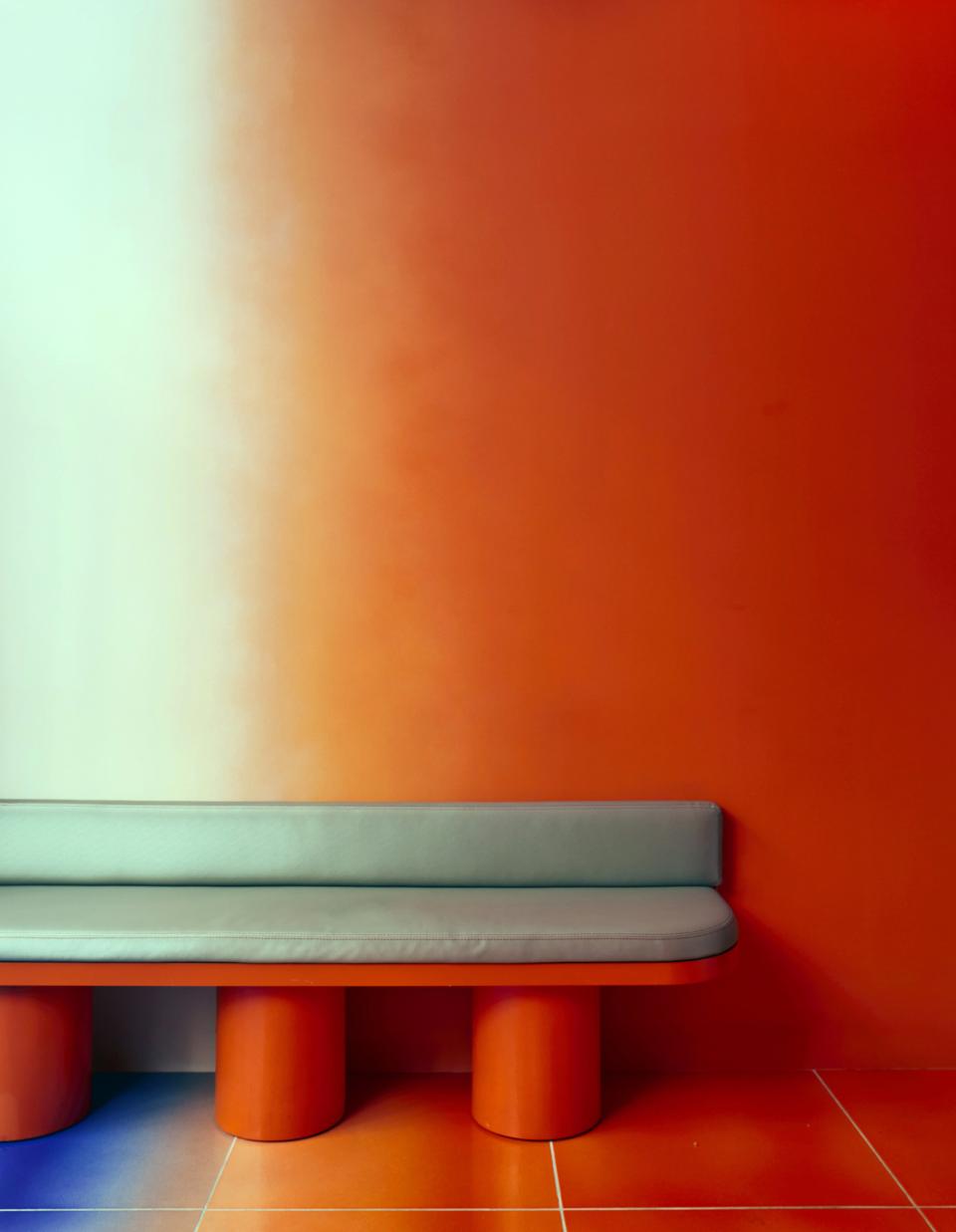 Vibrant orange wall with a sleek gray bench, showcasing psychedelic decor for Café Nuances by Uchronia.