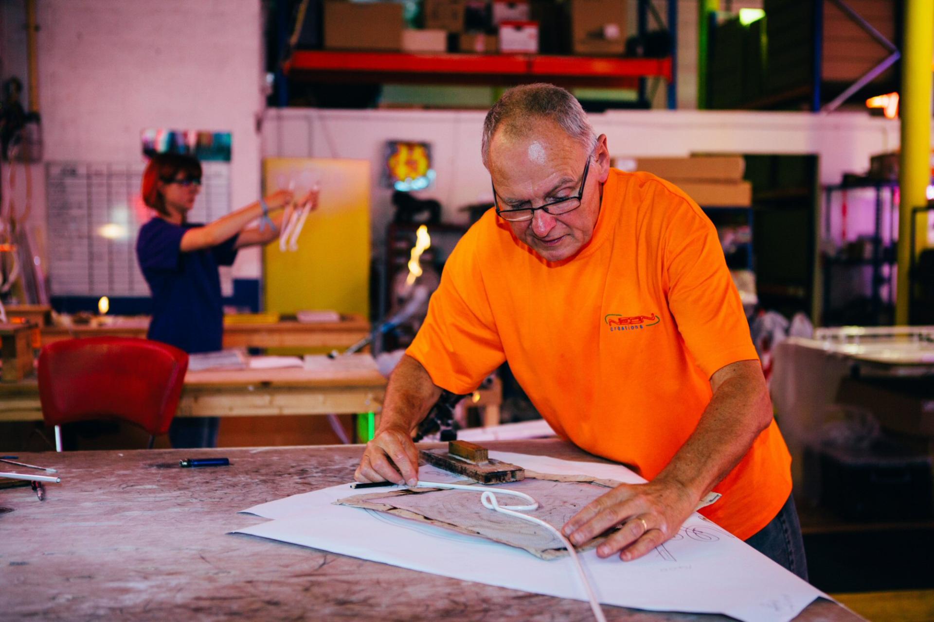 Workers shaping materials for neon sign production in a vibrant workshop, highlighting the craft of creating neon art.