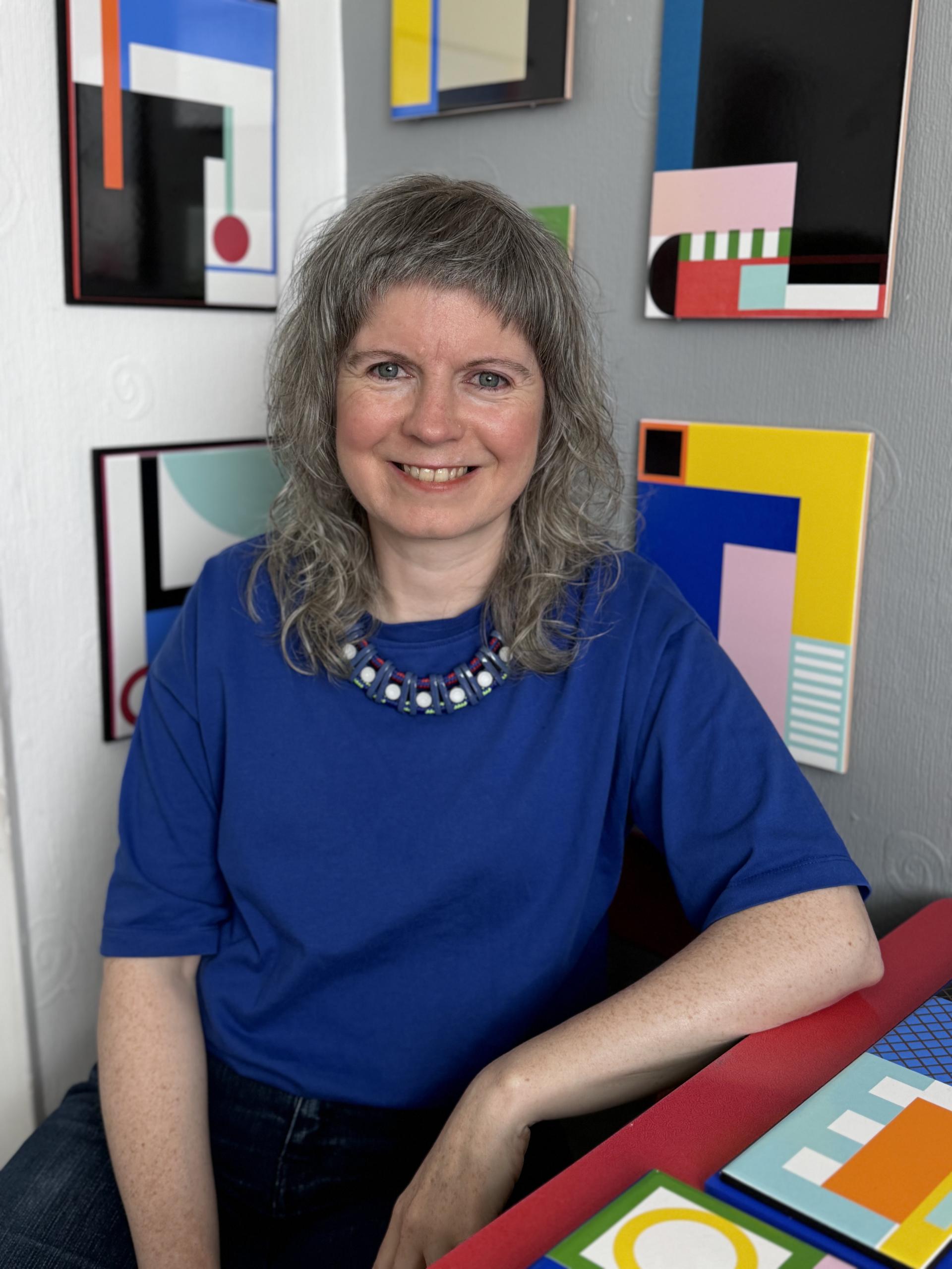 Laura Lightbody, a ceramic artist, smiles in front of her colorful enamel artworks, showcasing her unique artistic style.