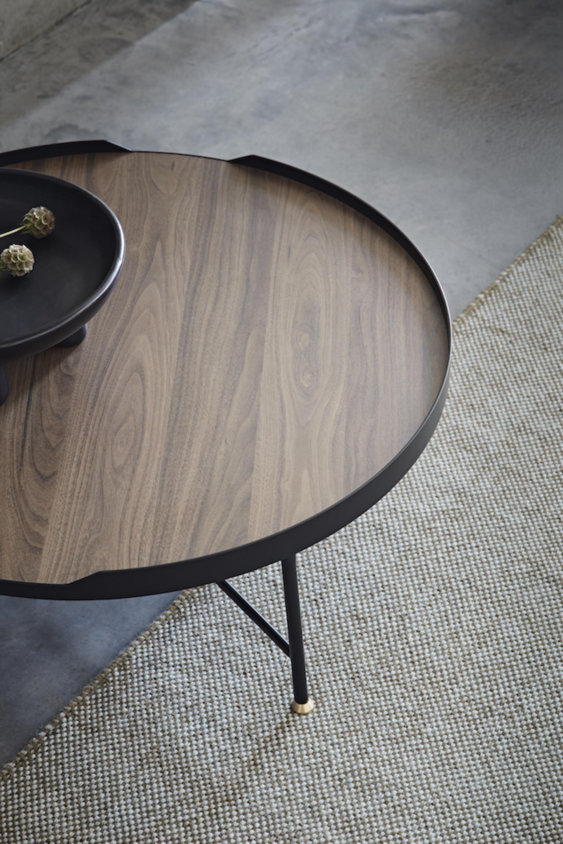 Stylish round coffee table featuring rich wood grain, black metal accents, and a textured rug beneath.