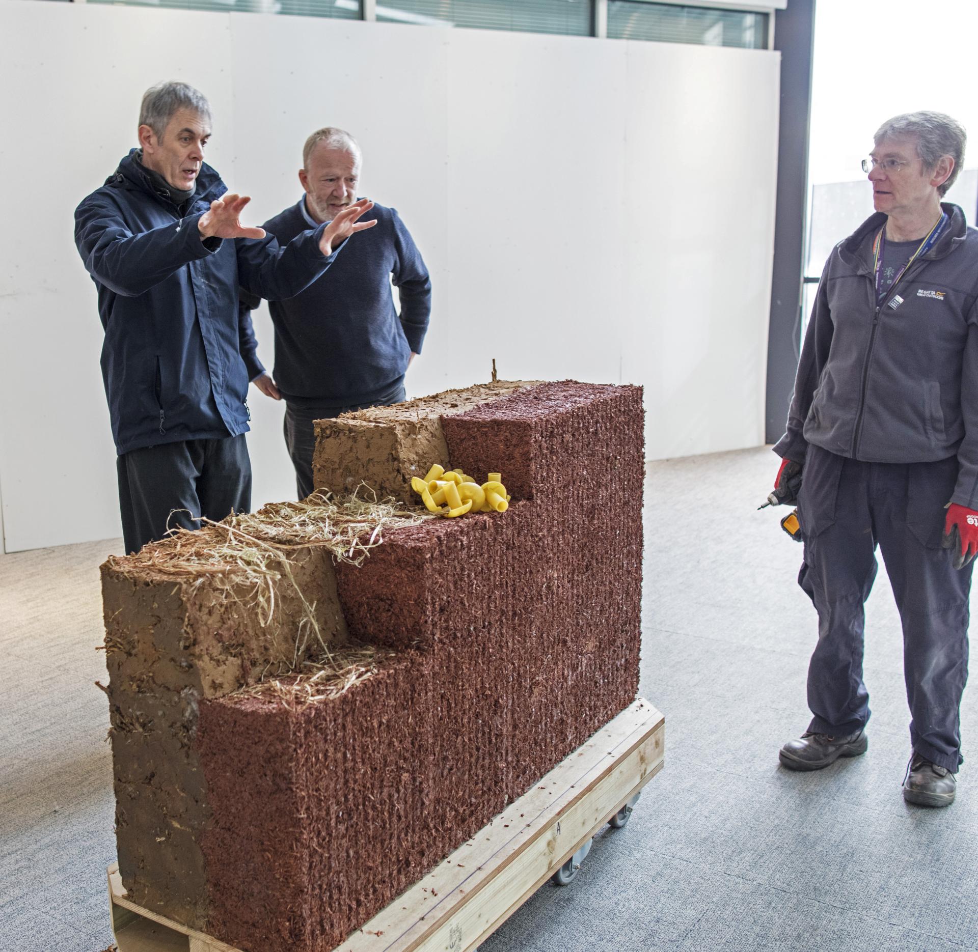 Researchers examine cob building materials made from earth and natural fibers during a study on sustainable construction techniques.