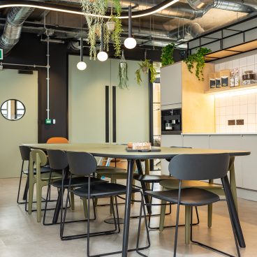Modern office space featuring a stylish dining table, black and olive chairs, and hanging plants, reflecting the Cadena House renovation.