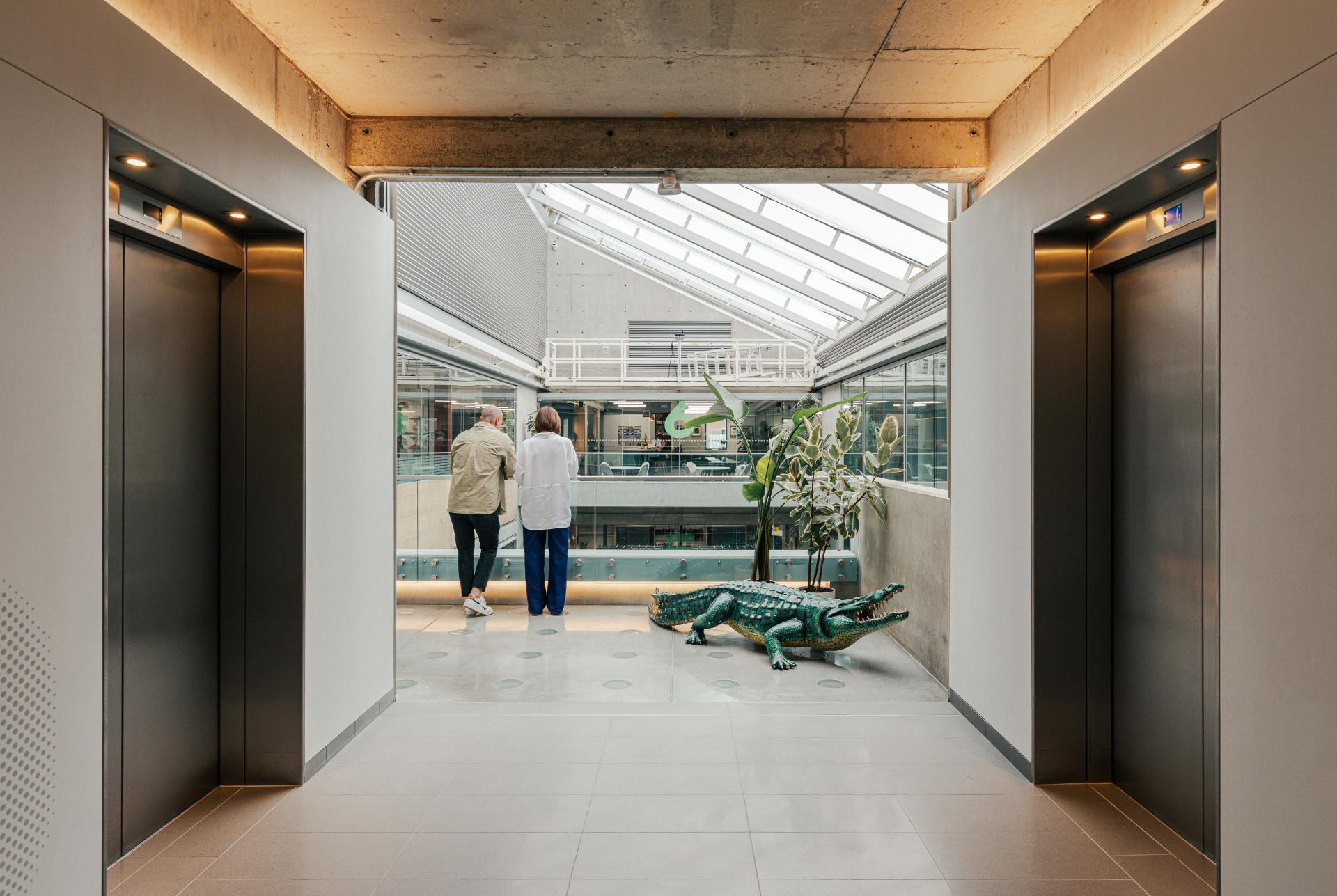Modern workspace design for Lacoste featuring a bright corridor, greenery, and artistic alligator sculpture.