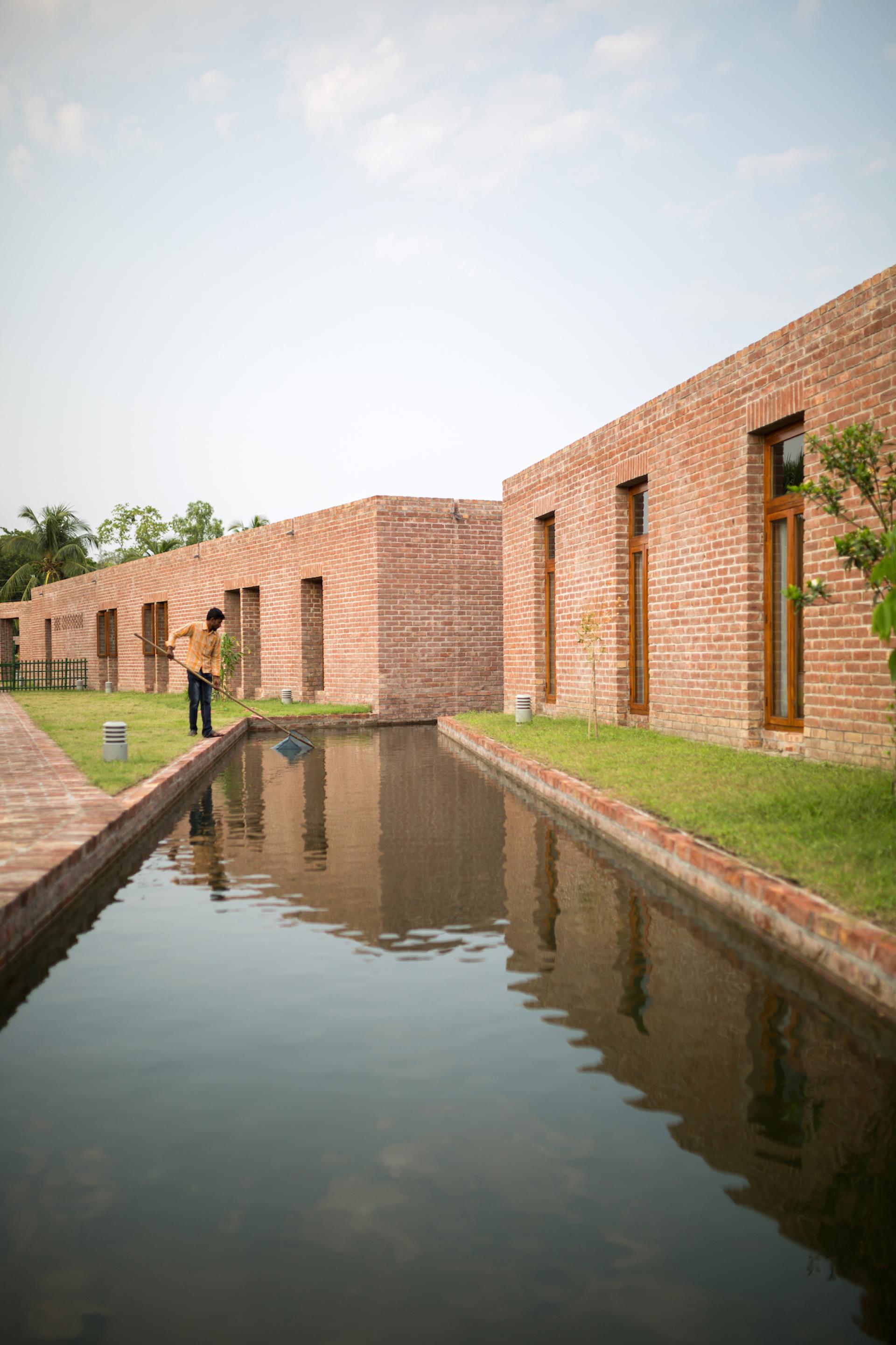 Remote community hospital in Bangladesh, featuring brick architecture and tranquil waterway cleaned by a caretaker.
