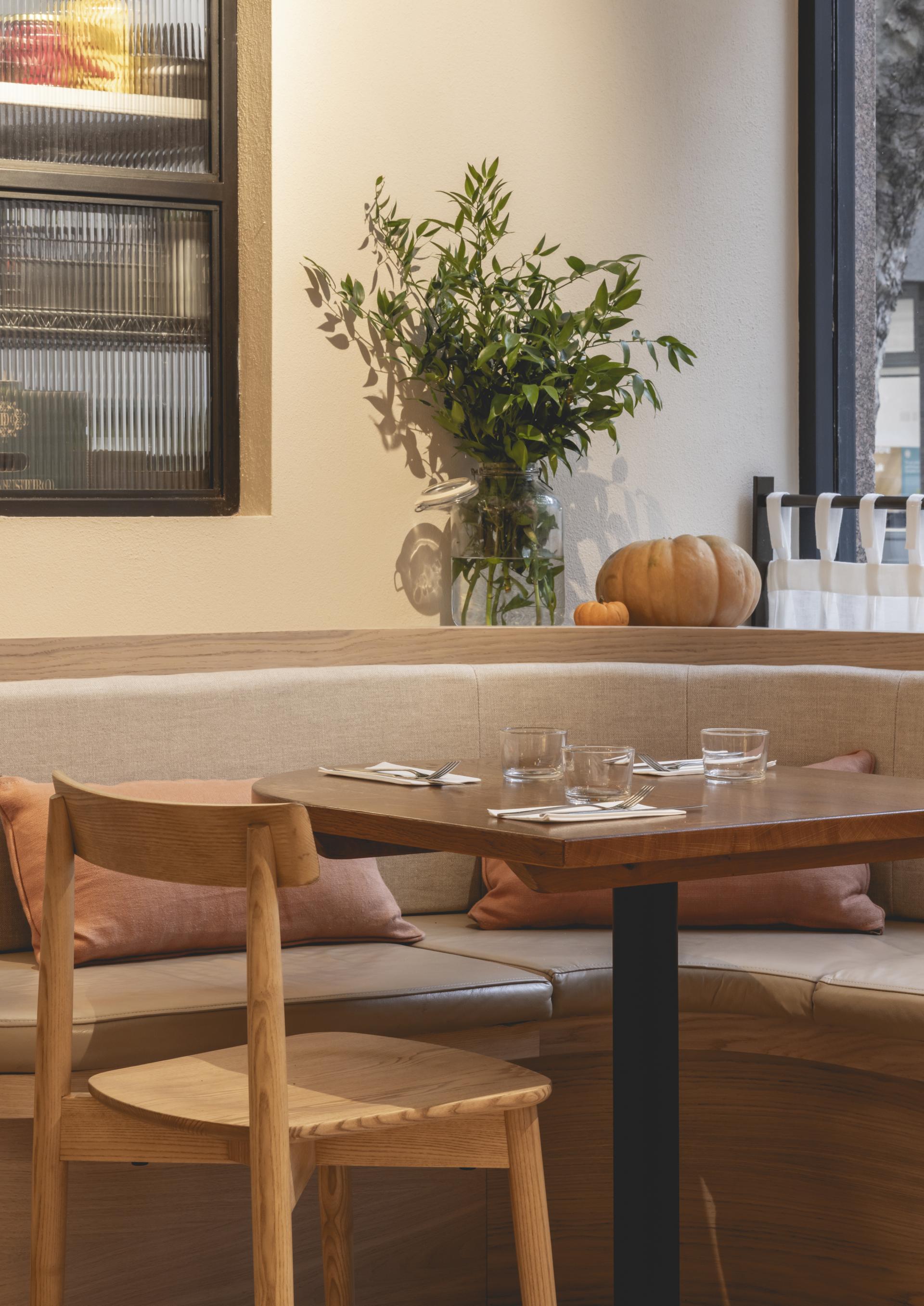 Welcoming interior of Honey & Co's deli featuring a wooden table, plush seating, and lush greenery accents.